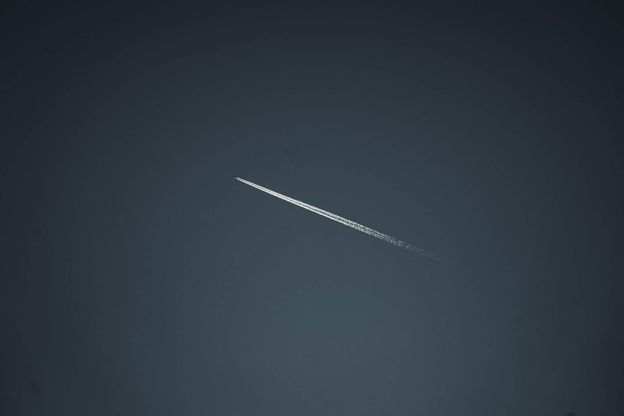 Airplane flying across a clear blue sky, leaving a white contrail behind it.