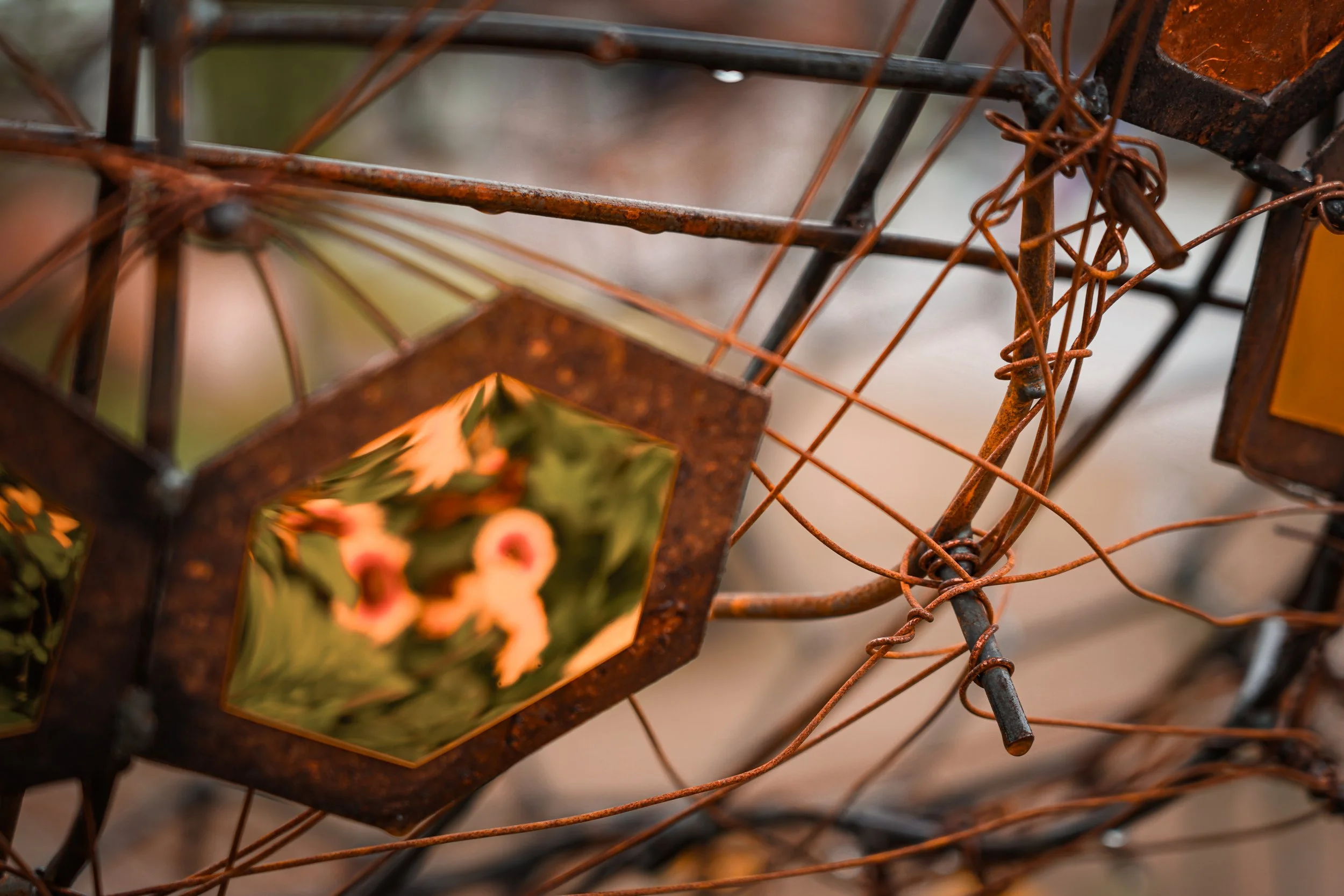 Close-up of a rusted metal wreath with a blurred ceramic ornament featuring a Christmas-themed design.
