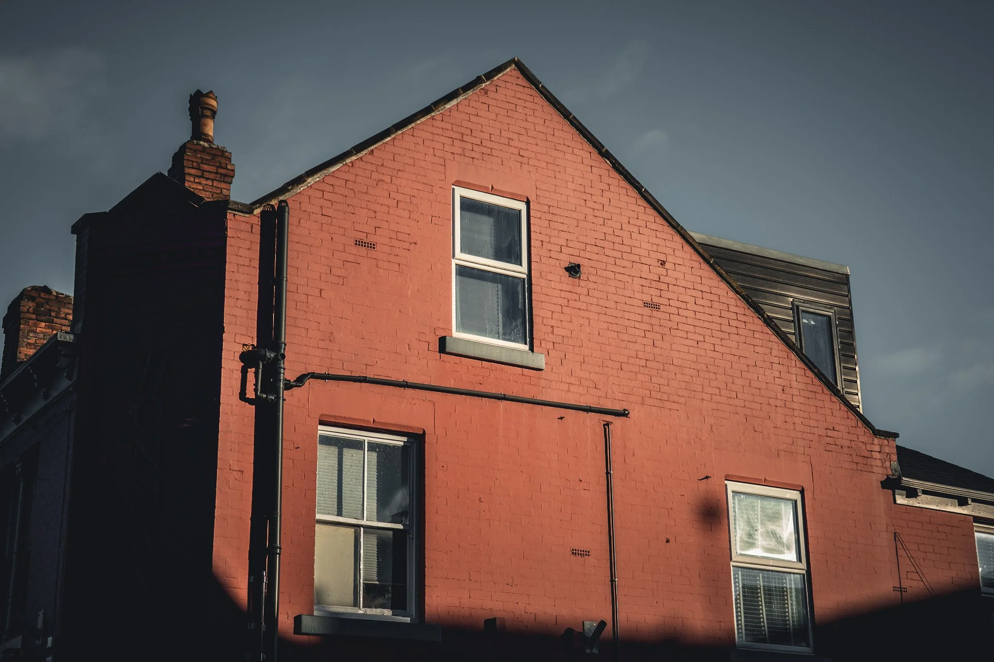 A red brick residential building with multiple windows under a cloudy sky.
