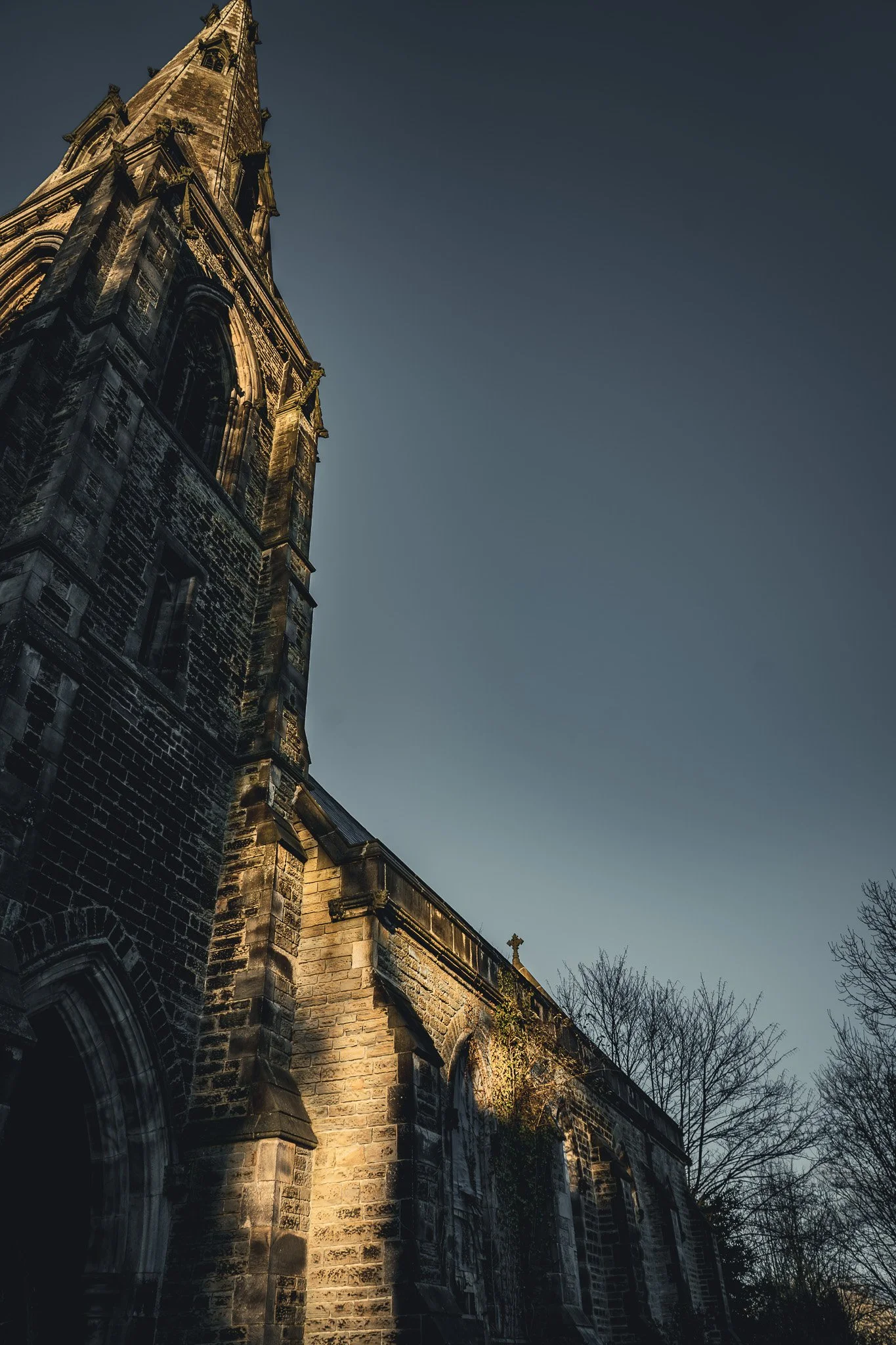 An old stone church with a tall steeple against a clear sky, surrounded by leafless trees.