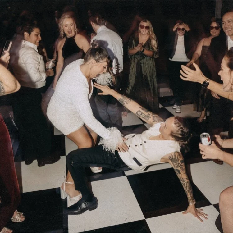 Two brides dancing together on a black and white checkered dance floor.