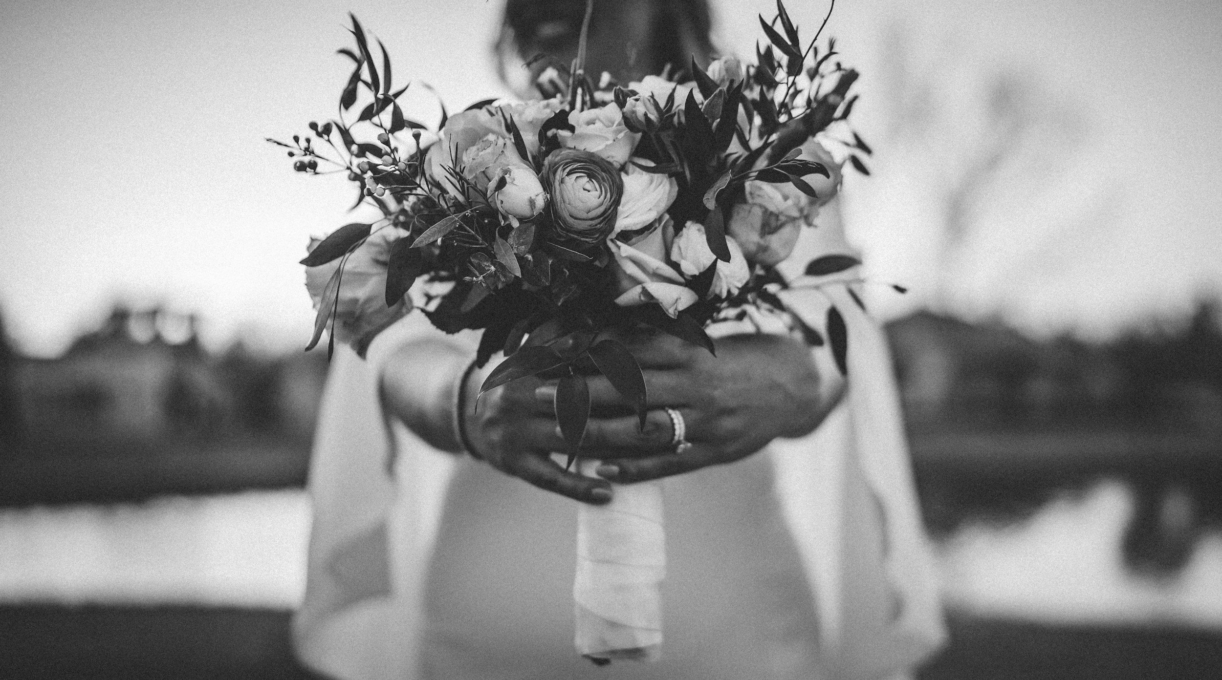 A person holding a bouquet of flowers, with focus on their hands and the flowers, in a black and white photo.
