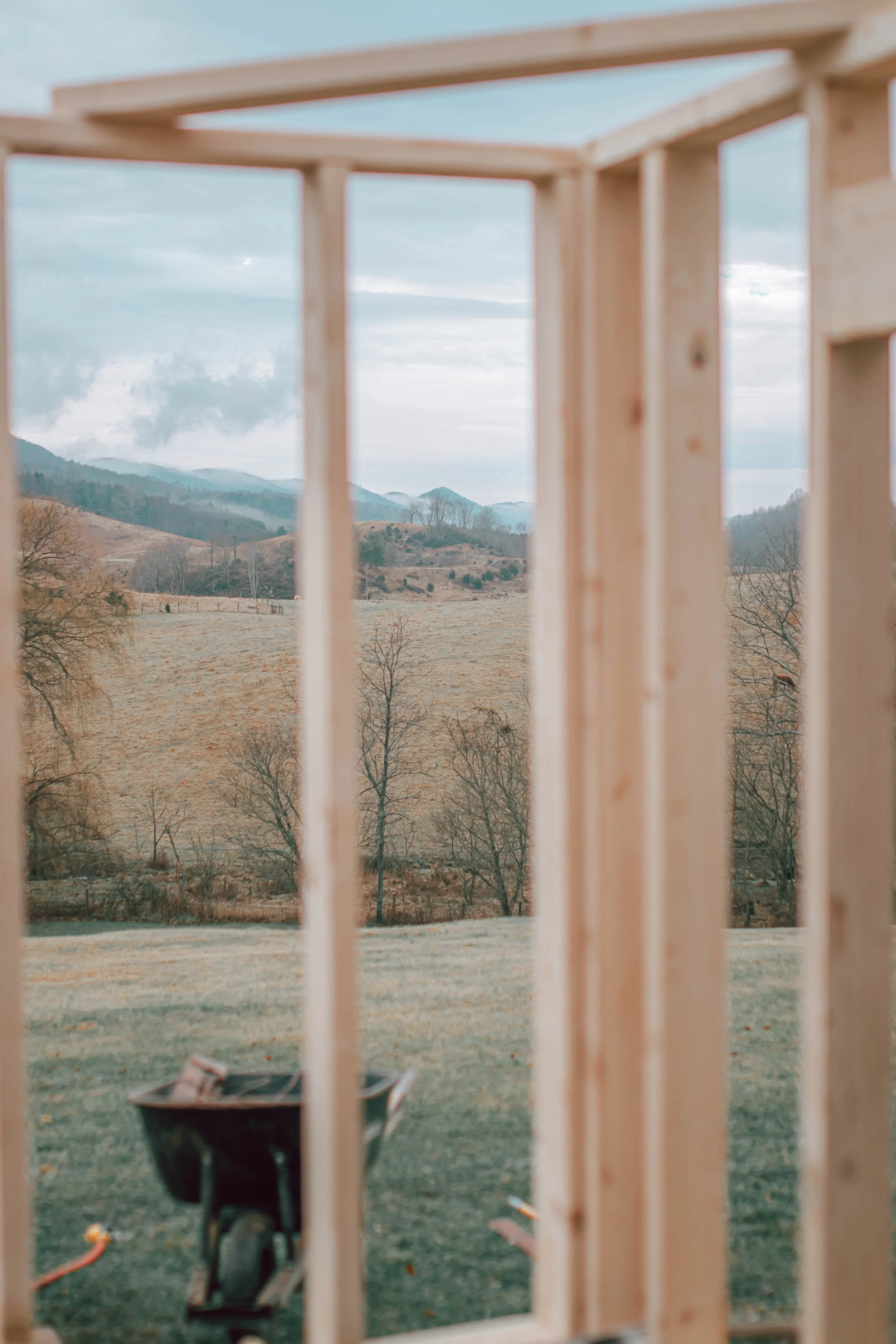 Wooden framing of a building under construction with a mountain landscape and cloudy sky visible through the opening.