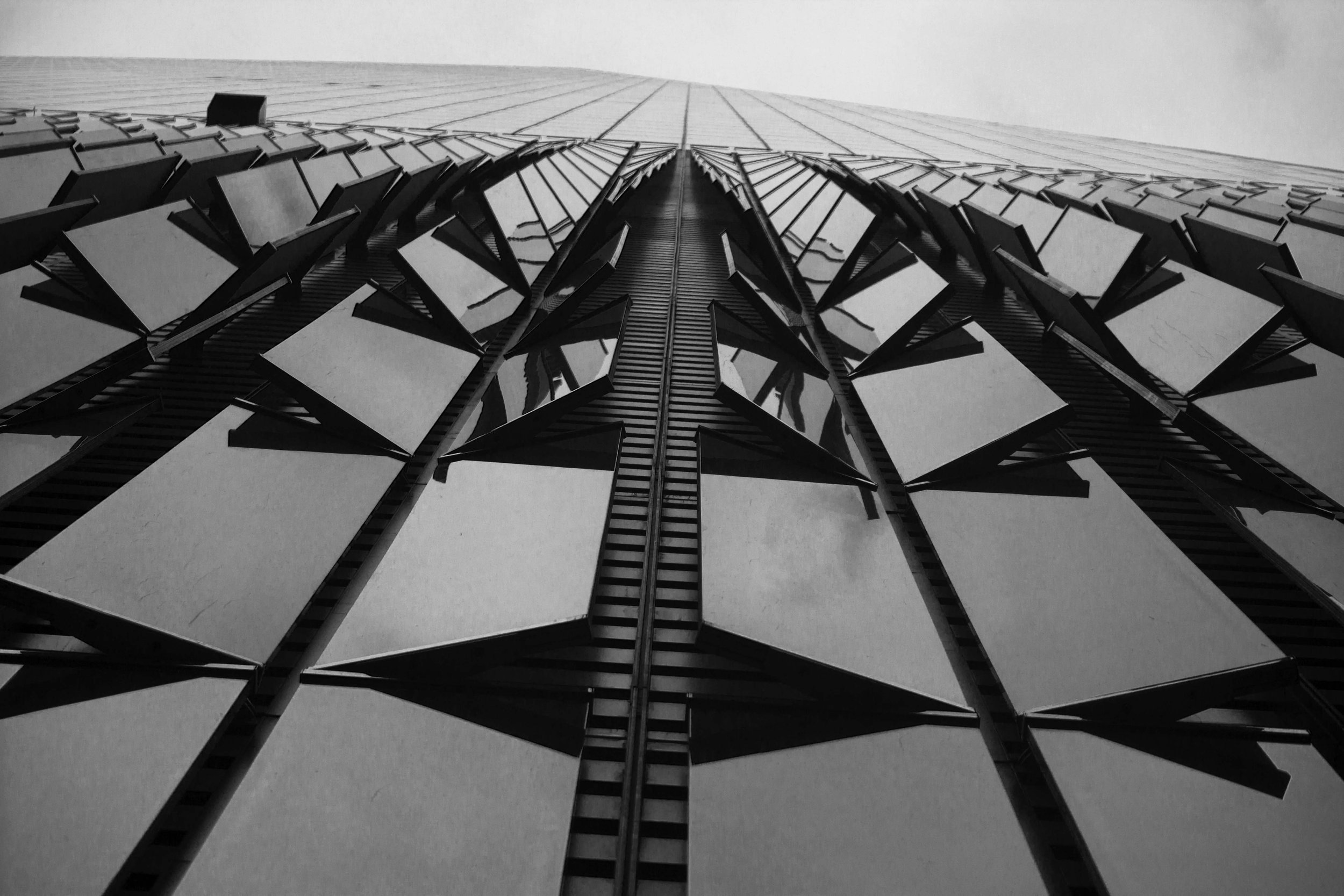 A black and white photo of a modern skyscraper taken from the ground looking up, showing windows and architectural details.