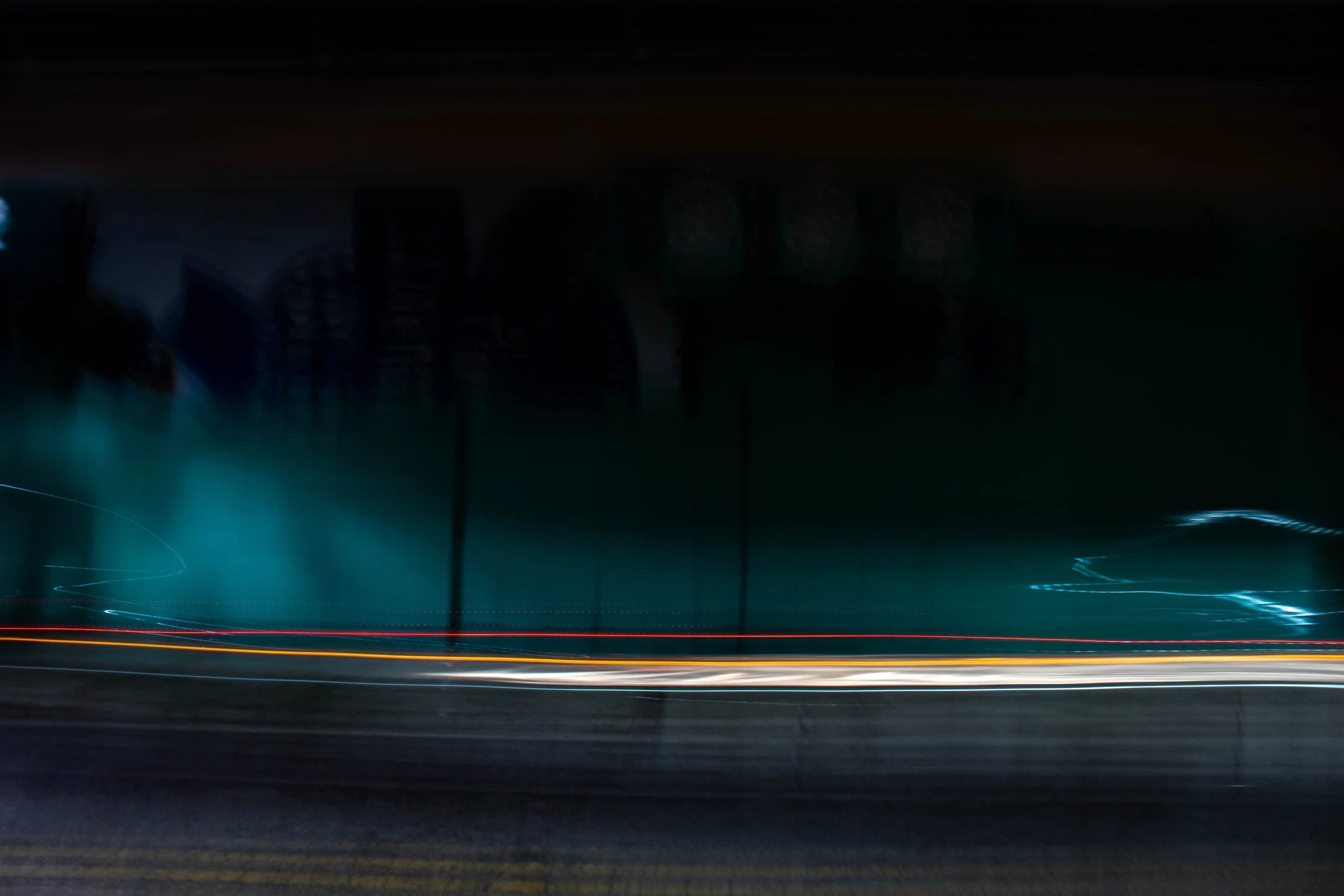Nighttime scene of a highway with light trails from moving vehicles, and illuminated signs above the road.