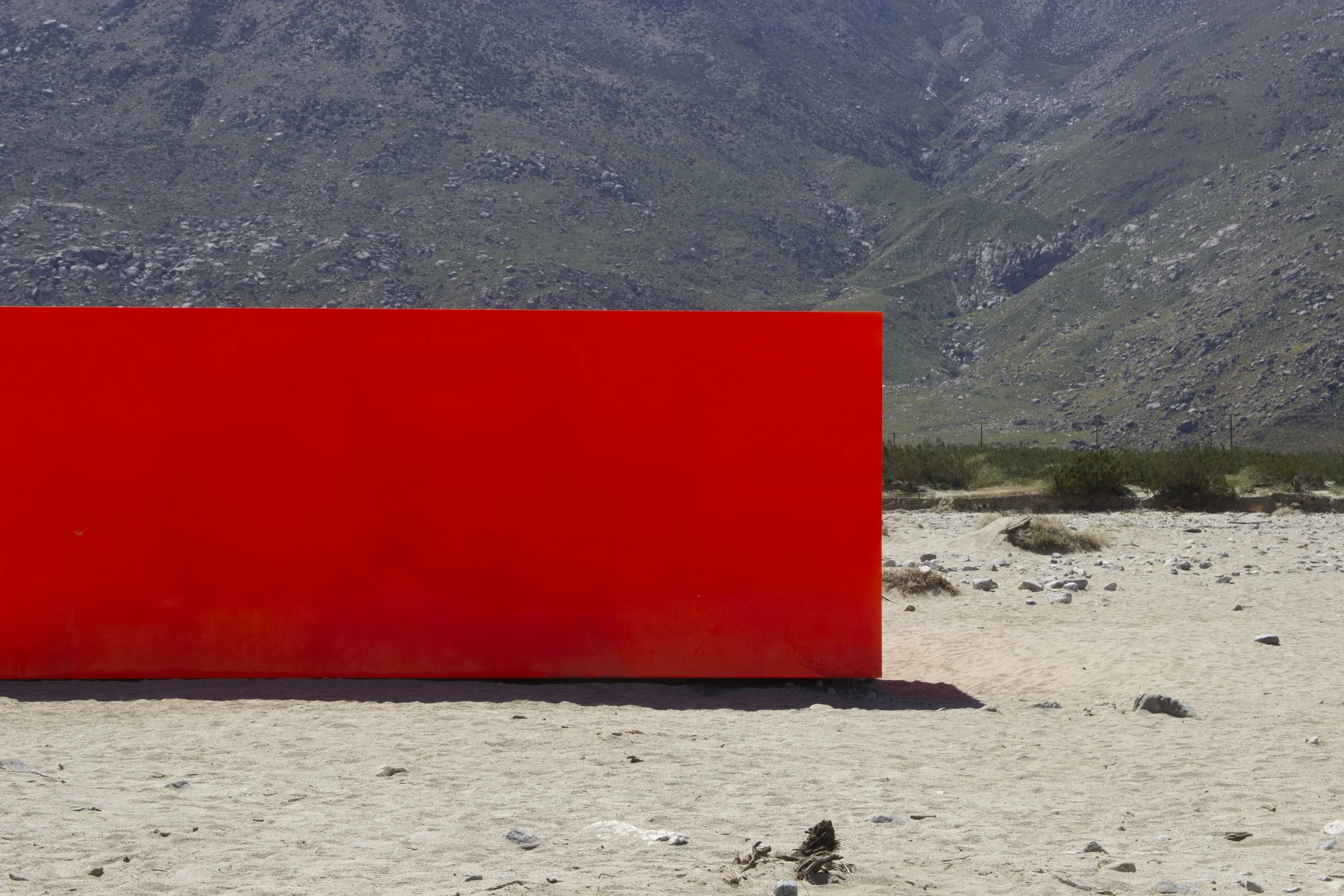 Large red rectangular sculpture in a desert area with mountains in the background