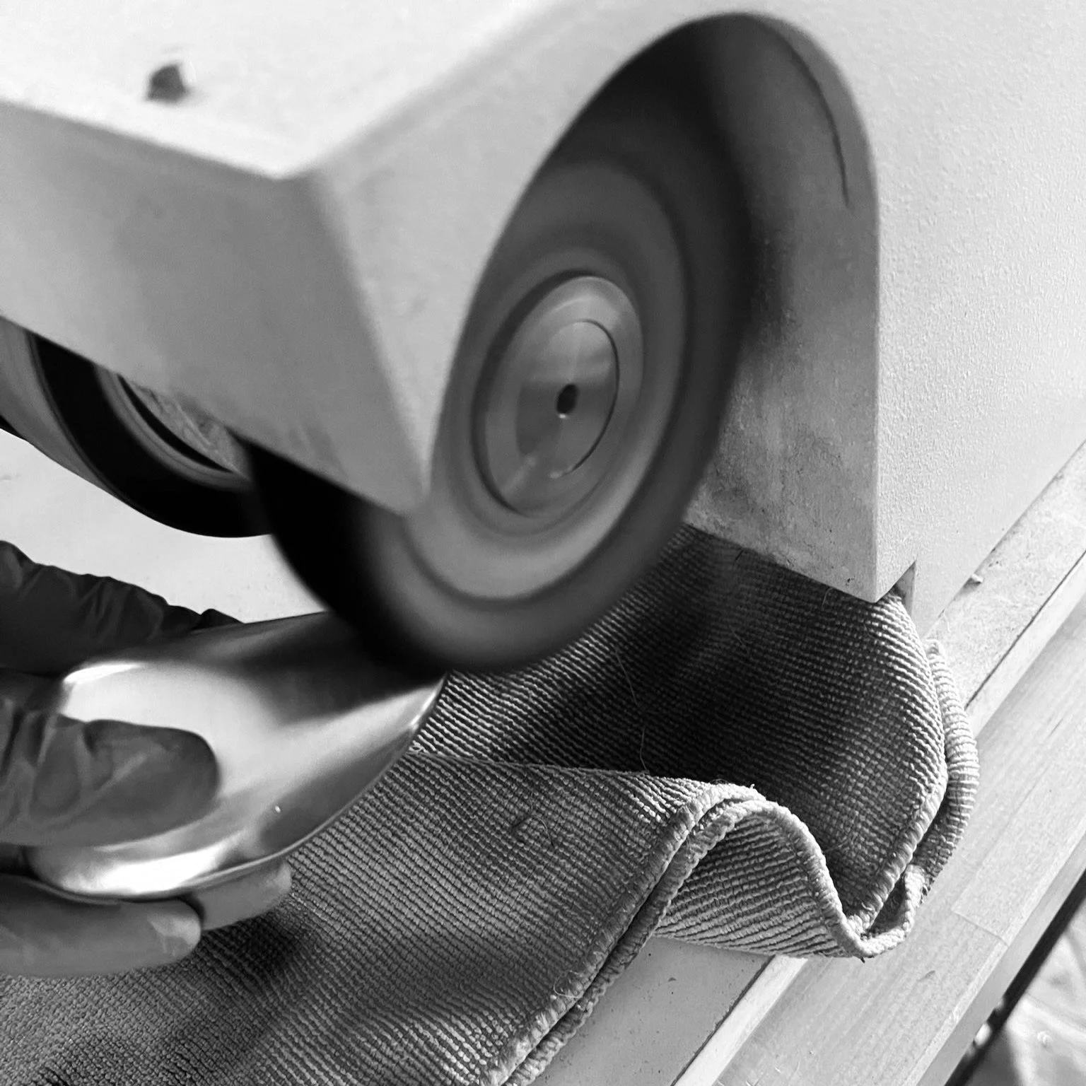 Close-up of a wheel grinding or sanding a metal object using a handheld tool, with a cloth underneath.