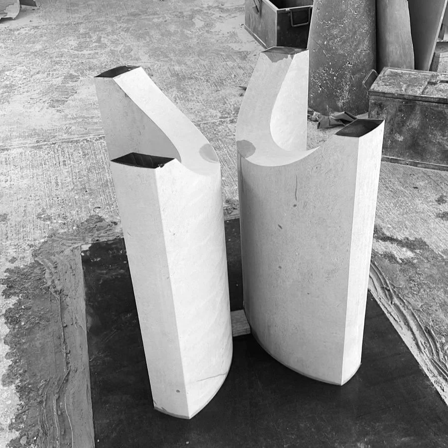 Two large, polished stone sculptures with curved shapes, standing upright on a rough concrete surface in a workshop or construction area.