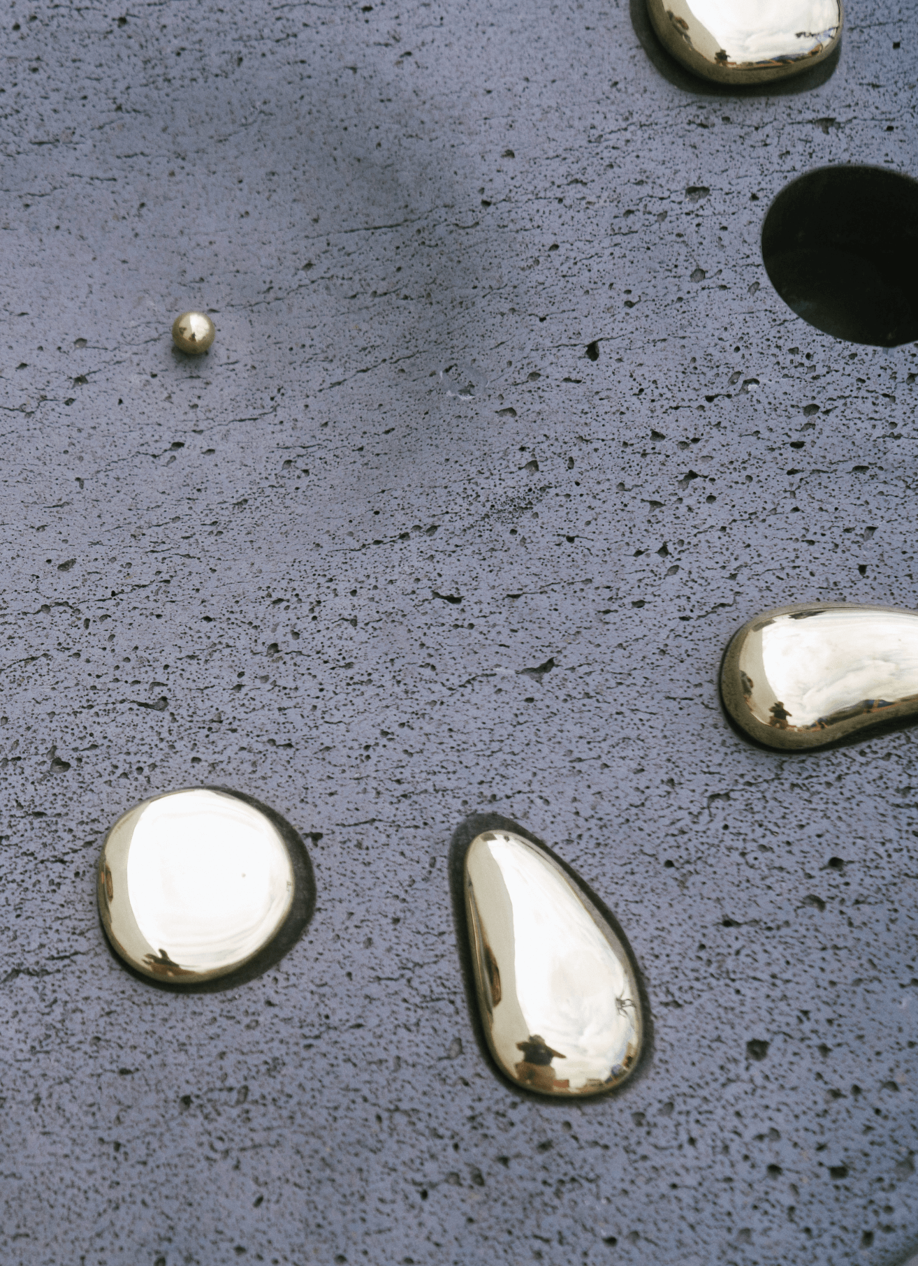 Close-up of a textured black surface with shiny, metallic gold drops and a gold ball, and part of a gold-colored object.