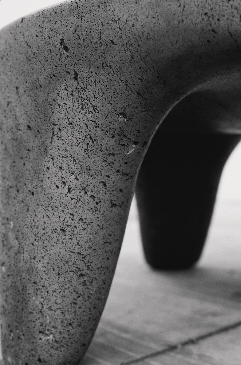 Close-up of a textured concrete or stone sculpture or object with a curved shape, resting on a wooden surface.