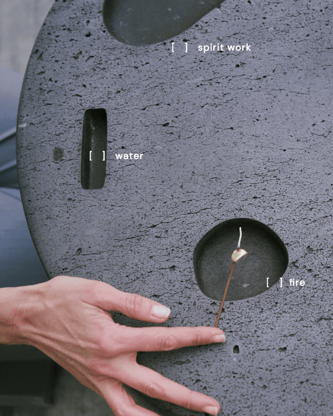 A concrete fire safety testing device with labeled compartments for water, spirit work, and fire; a person's hand is near the fire compartment, holding a lit match.