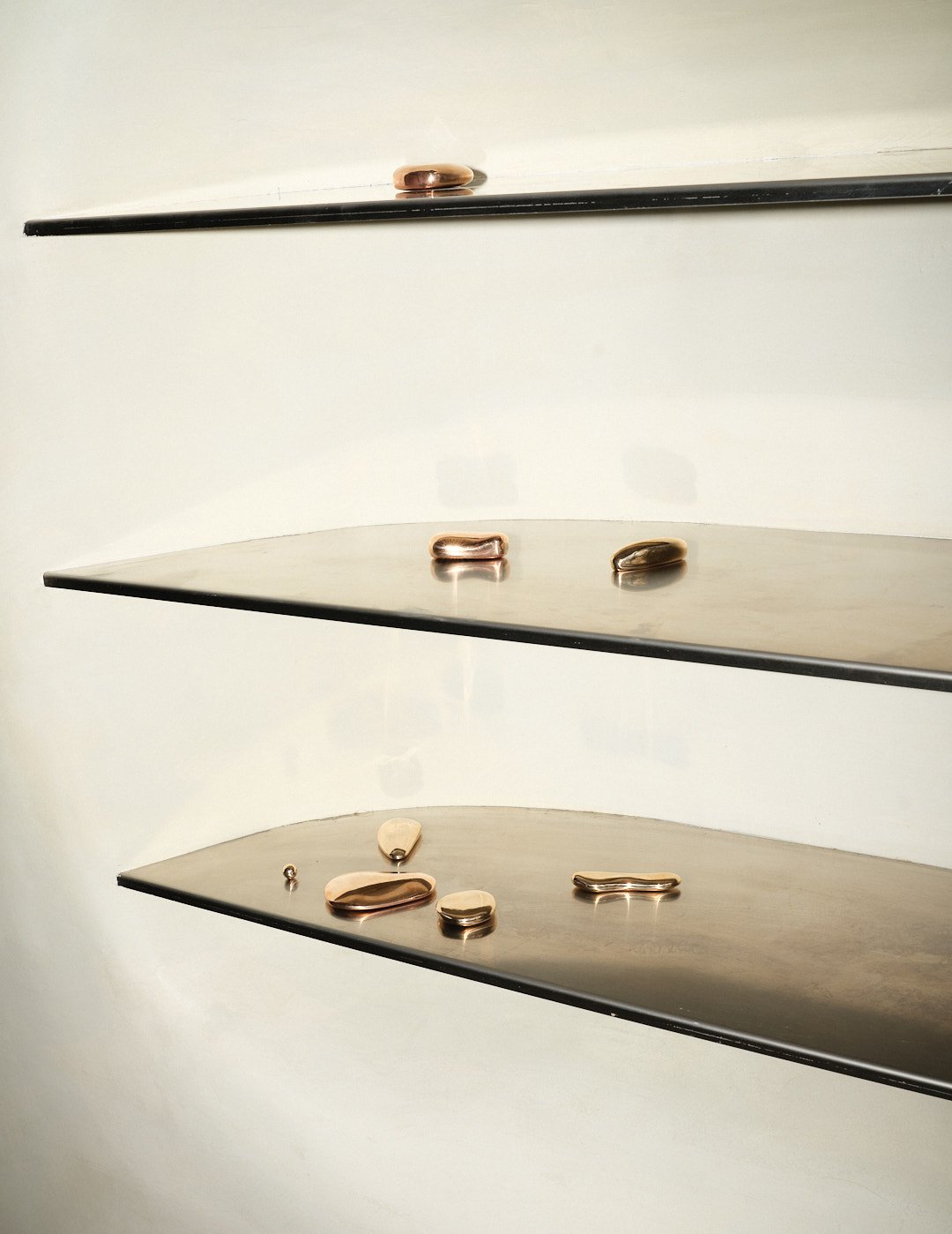 Three black shelves with various jewelry pieces, including rings and earrings, displayed on each shelf against a plain background.