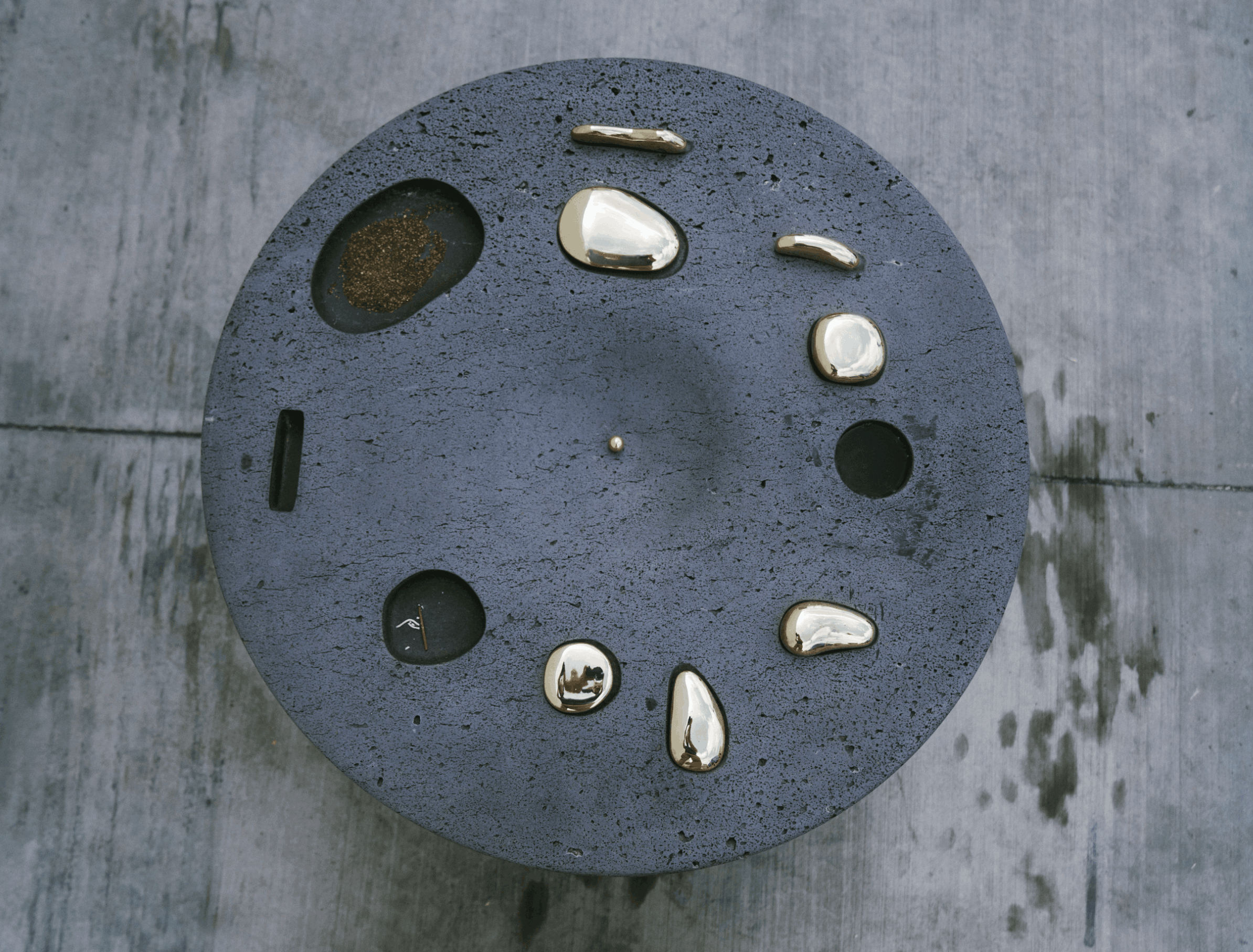 Round black textured clock with gold and white markers, no visible hands, on a gray wooden surface.
