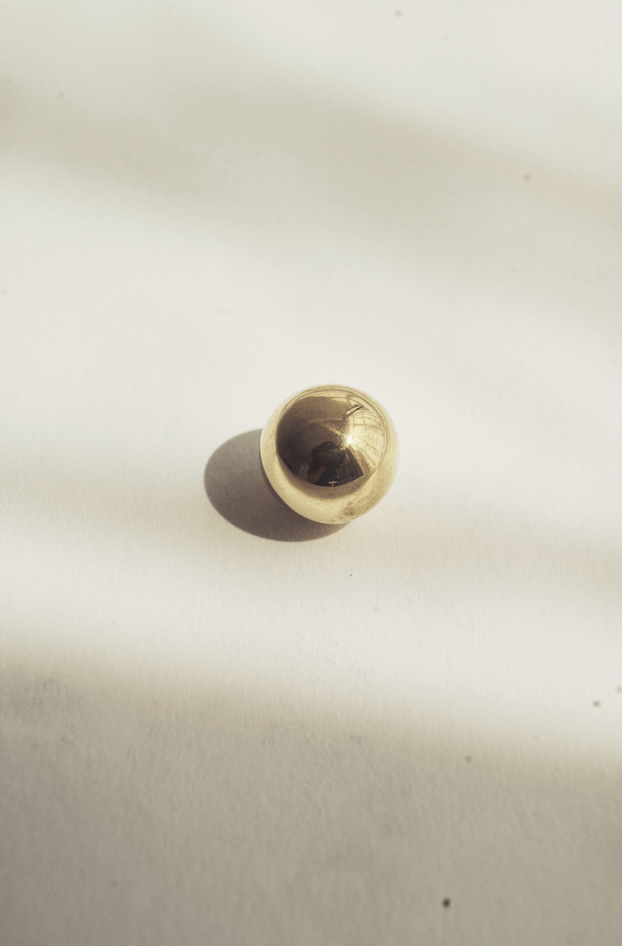 A shiny, round, metallic object, possibly a ball, sitting on a white surface casting a shadow.