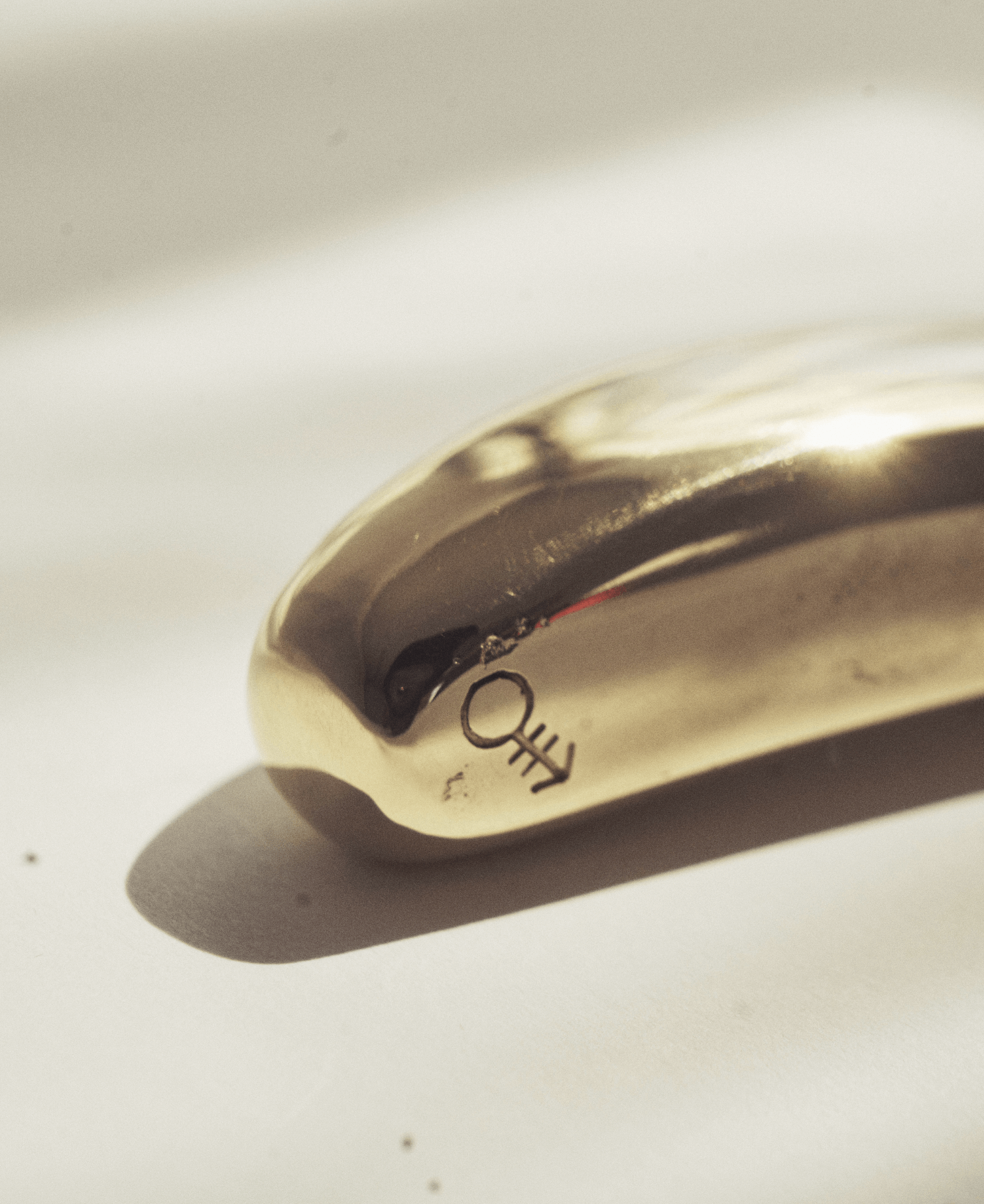 Close-up of a metallic bottle opener with the word 'LOOT' engraved on it, casting a shadow on a white surface.
