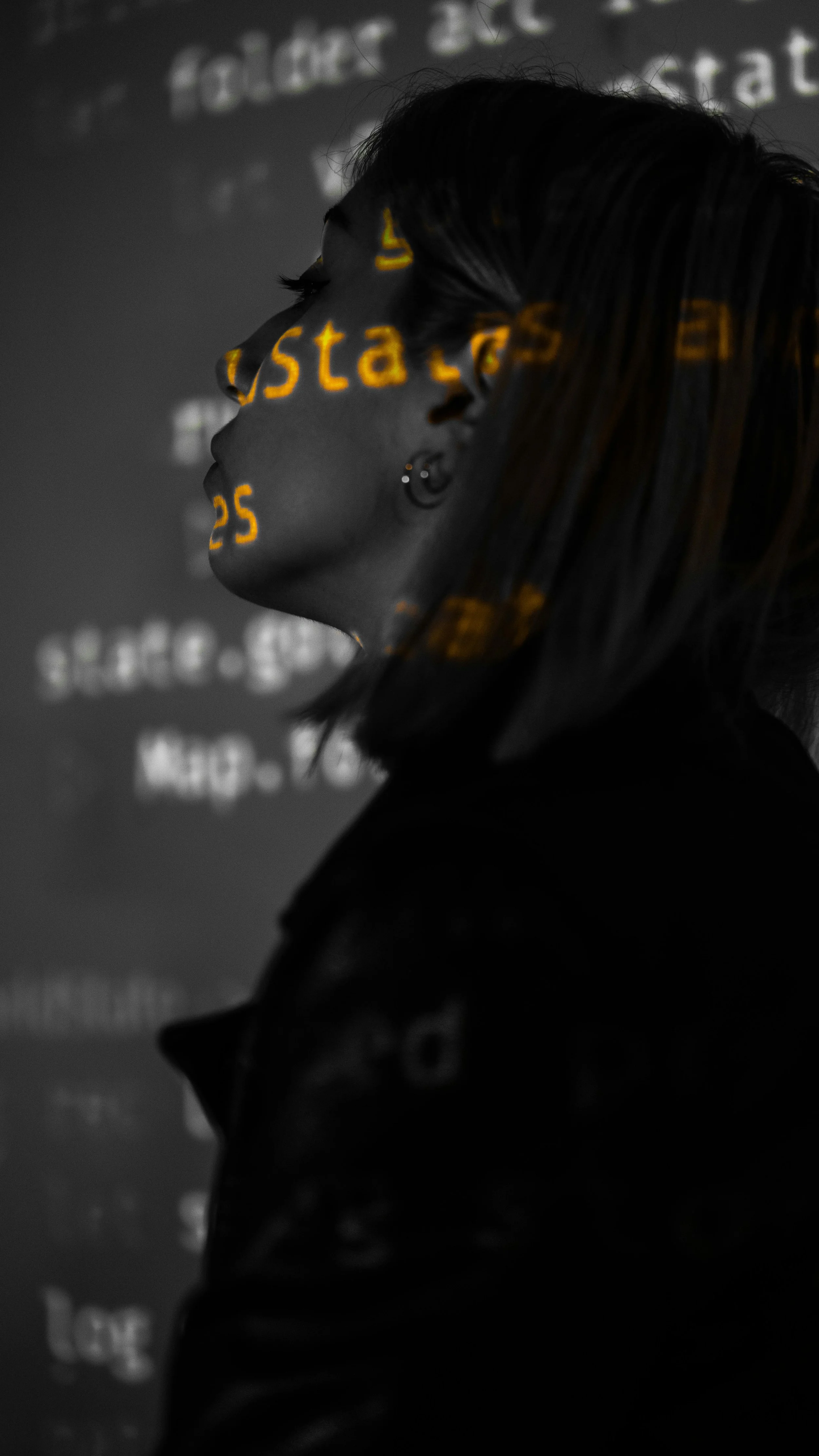 A young woman is standing side on and her face is covered in shadow and bright text from a computer projector is covering her face.