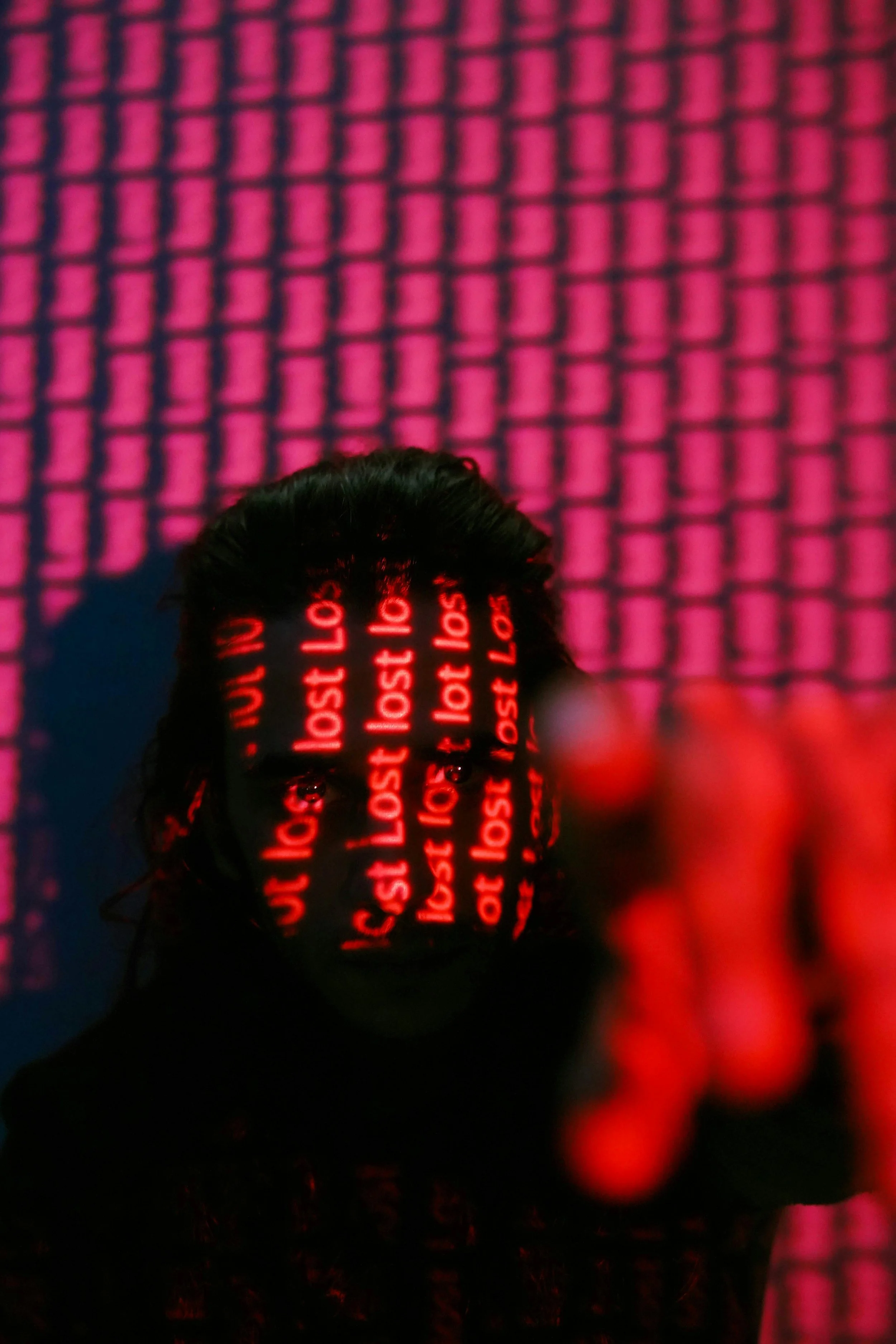 A high angle image of a young man covered in shadow and read lights that read "Lost lost lost." He is pointing his finger at the camera.