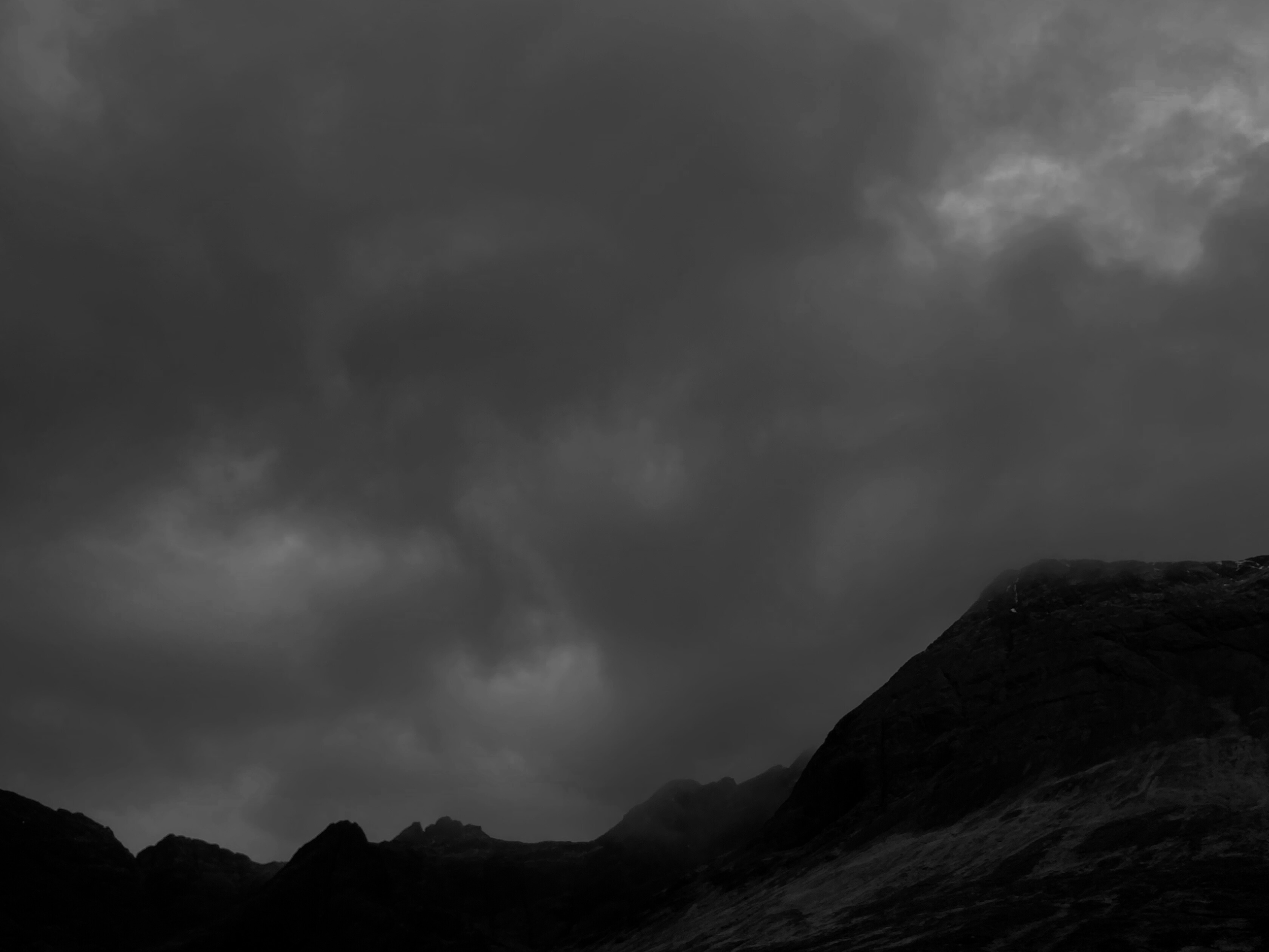 Dark, cloudy sky over a mountain landscape with rugged terrain in black and white.