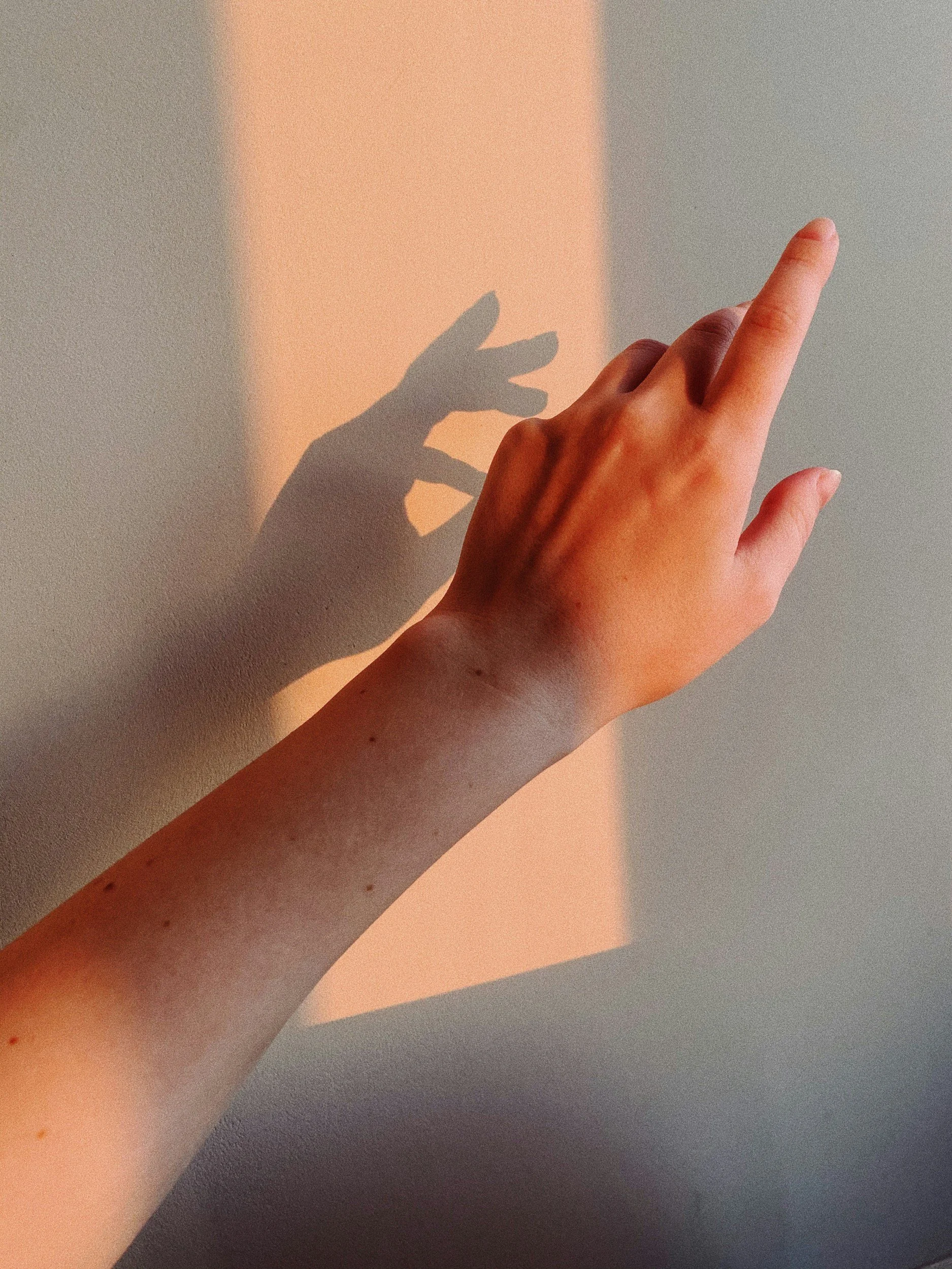 A person's hand with fingers extended, casting a shadow on a wall, with warm and cool colored light in the background.