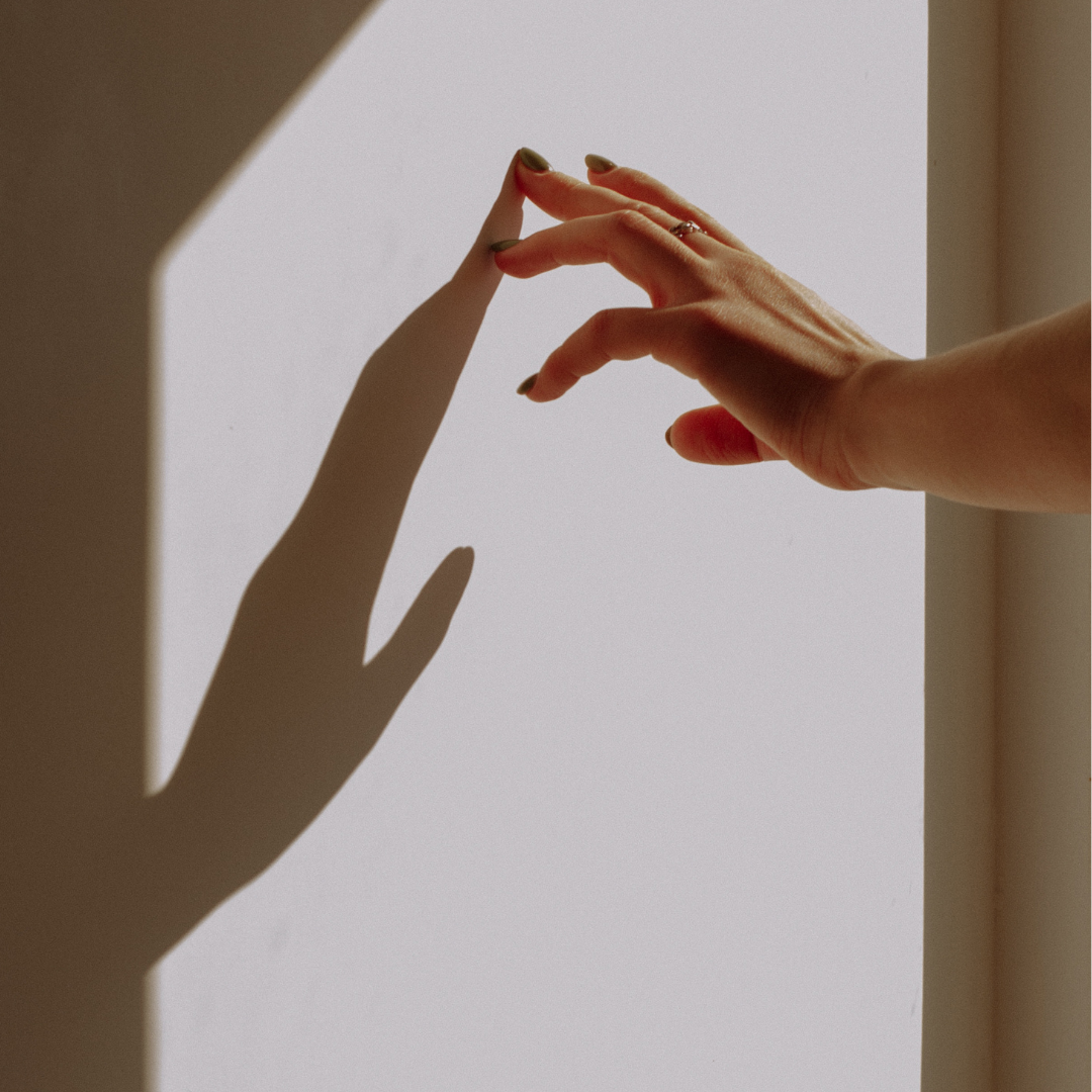 A hand reaching toward its own shadow on a wall, with the shadow mirroring the hand's position and fingers.