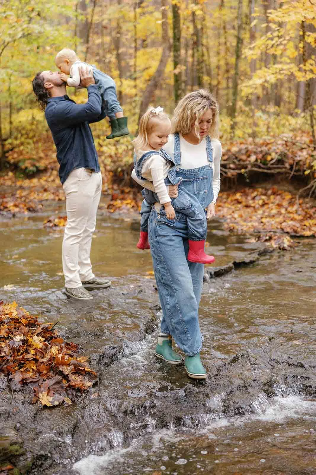 Family of four in fall outfits walking across a stream in Tennessee