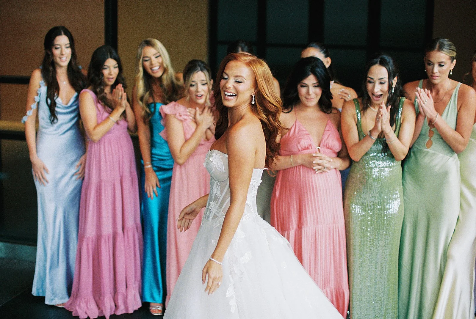 Bride in wedding dress dancing while her bridesmaids in colorful dresses watch and smile.