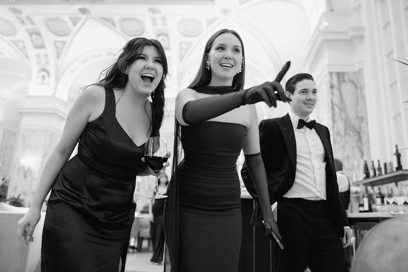 Black and white photo of three wedding guests smiling and staring at something in the distance while pointing