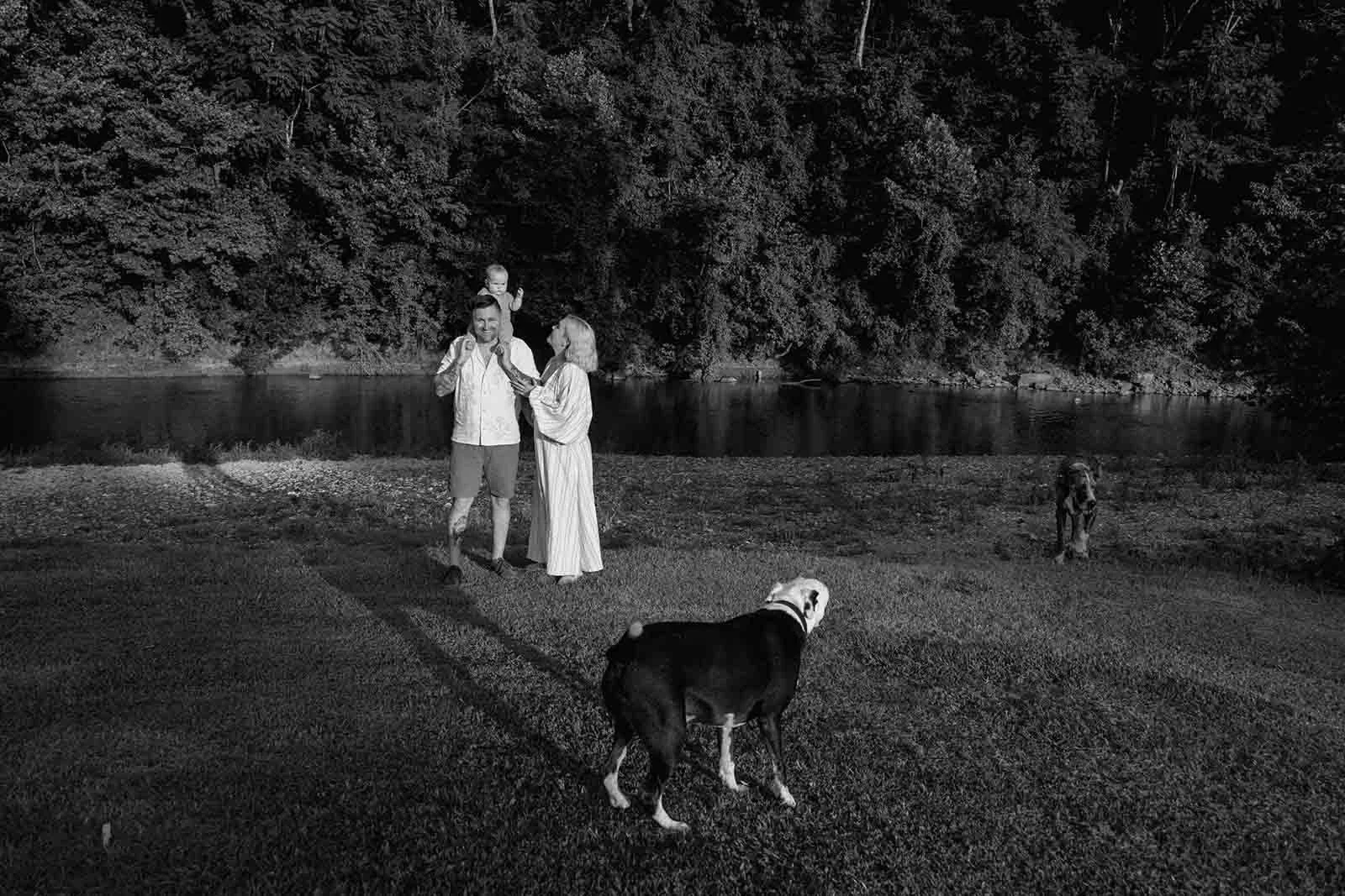 Black and white photo of a family of three playing near the shore with a dog running around