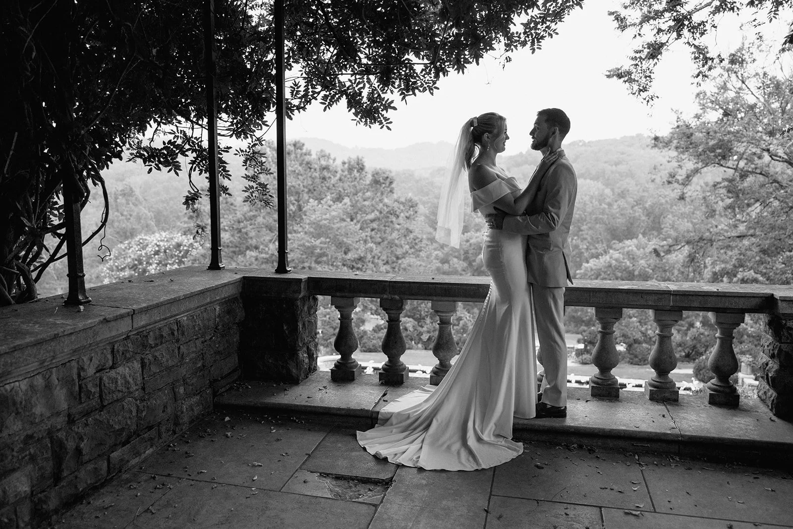 Black and white photo of bride and groom holding each other on a balcony at Cheekwood Gardens