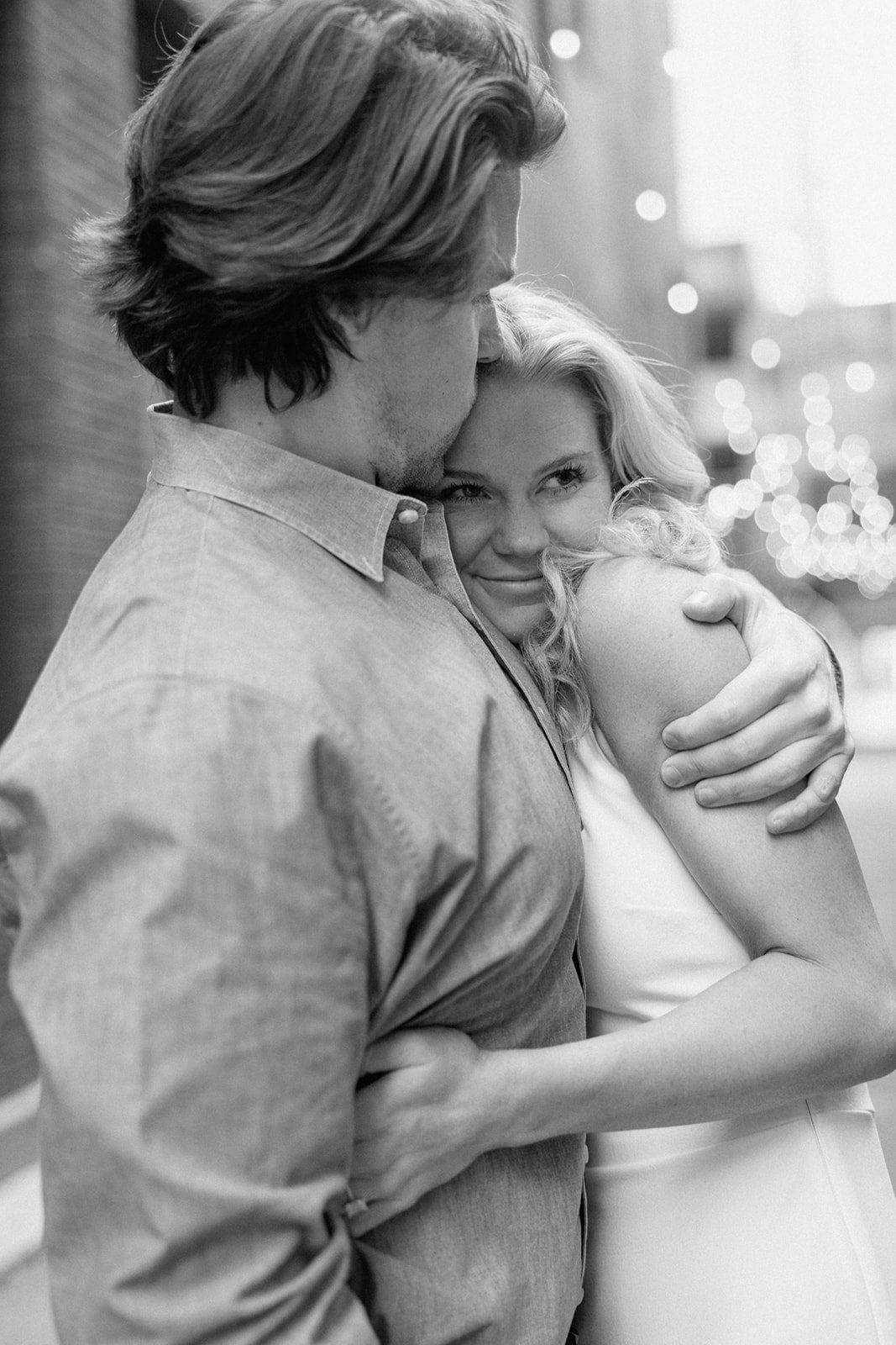 Man hugs woman and kisses her forehead in downtown engagement photo
