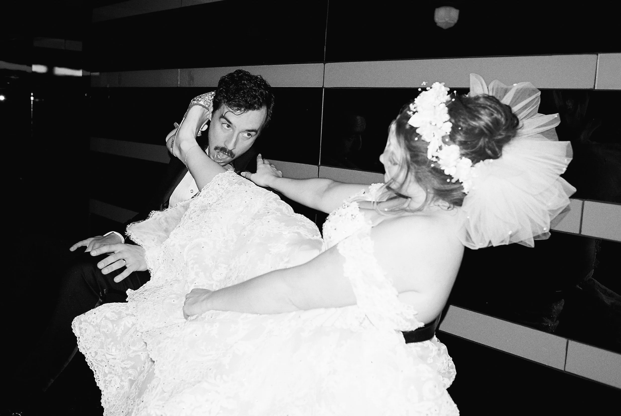 Black and white photo of a bride hooking the groom's face with her heel and leaning back