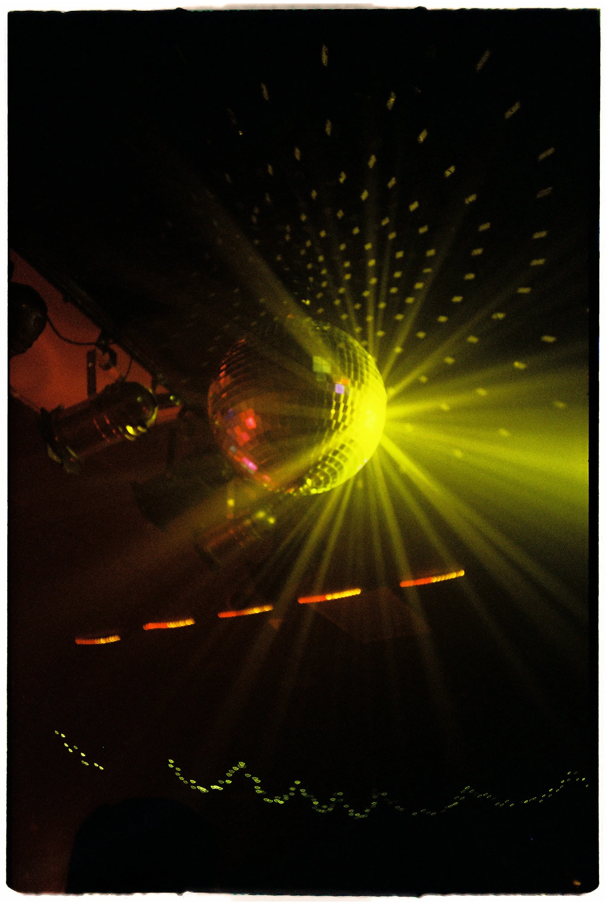 A disco ball reflecting yellow lights on a dark ceiling, creating a pattern of small light spots.