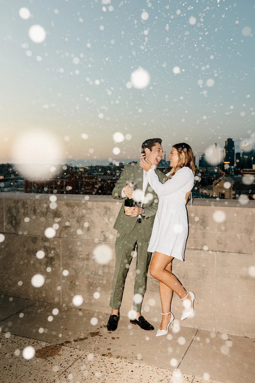 couple kissing on a rooftop of a parking garage spraying champagne for their engagement photos