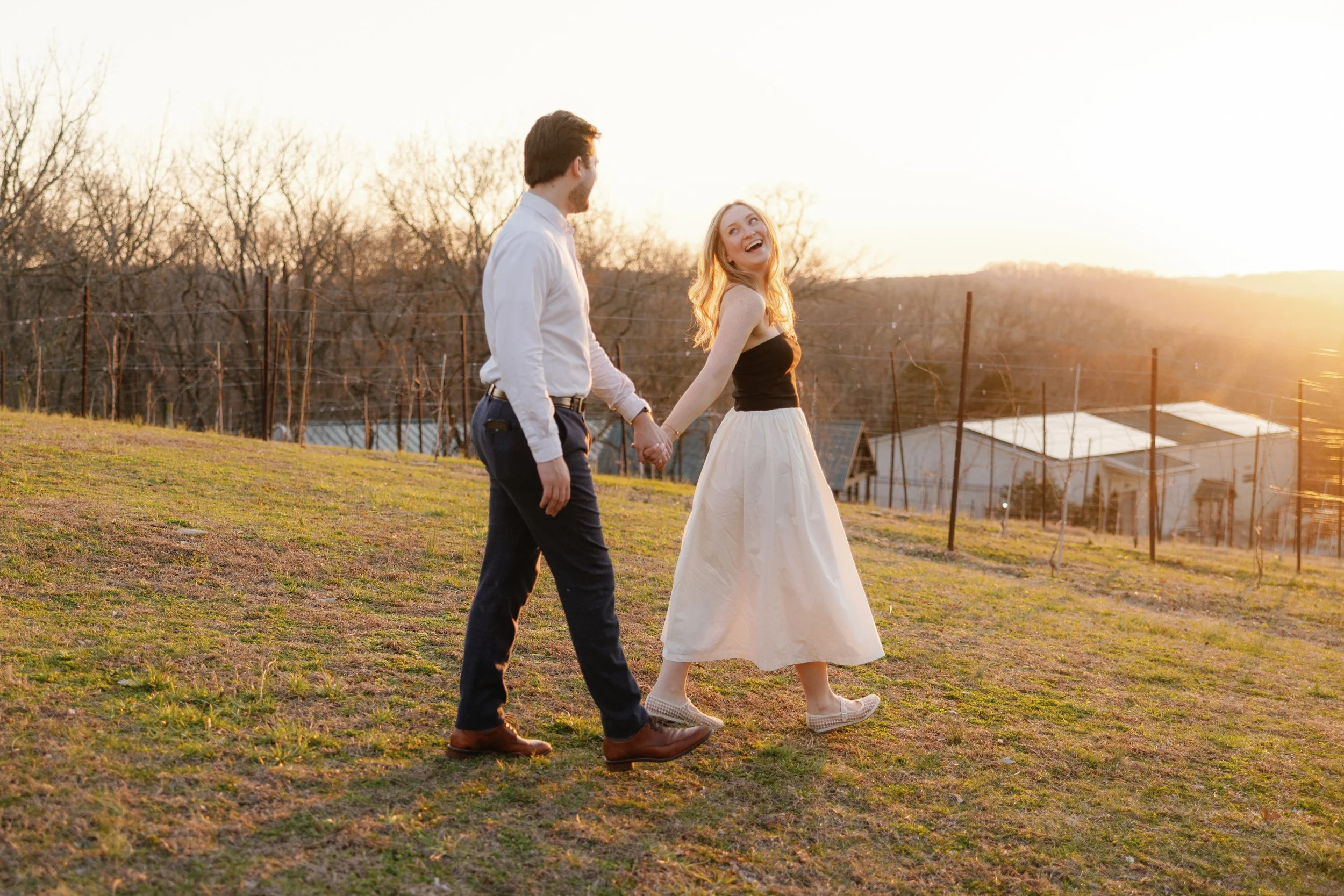 Man and woman walk on a grassy hill for their engagement photos