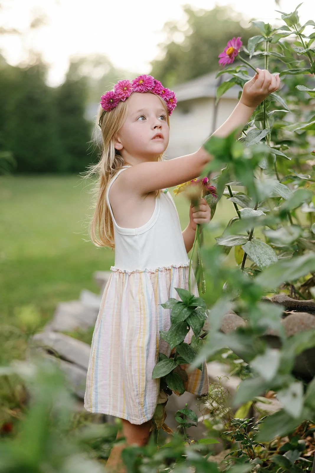 Little girl in a flower crown picking flowers from vines