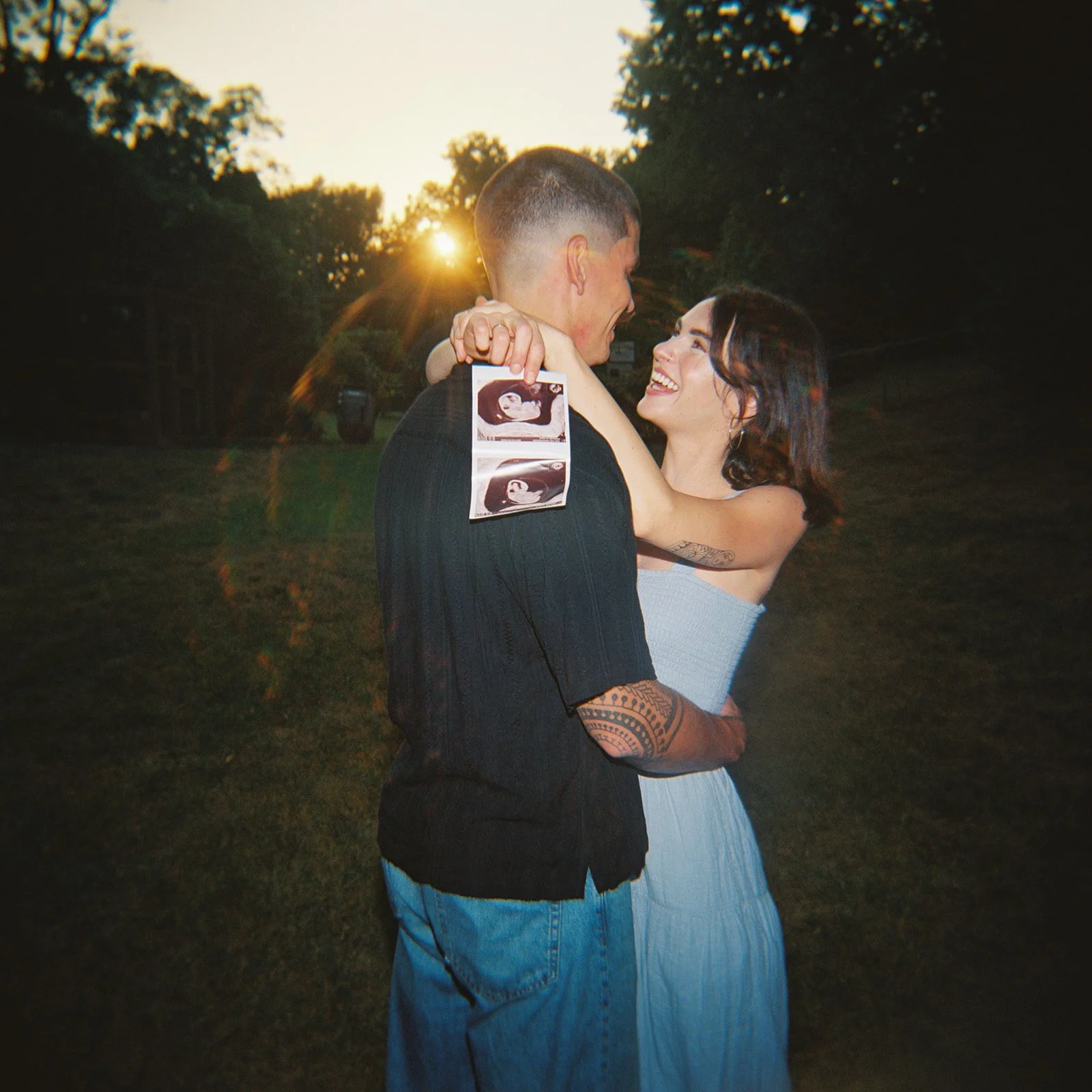 Husband and wife under the sunset embracing while holding their ultrasound photos