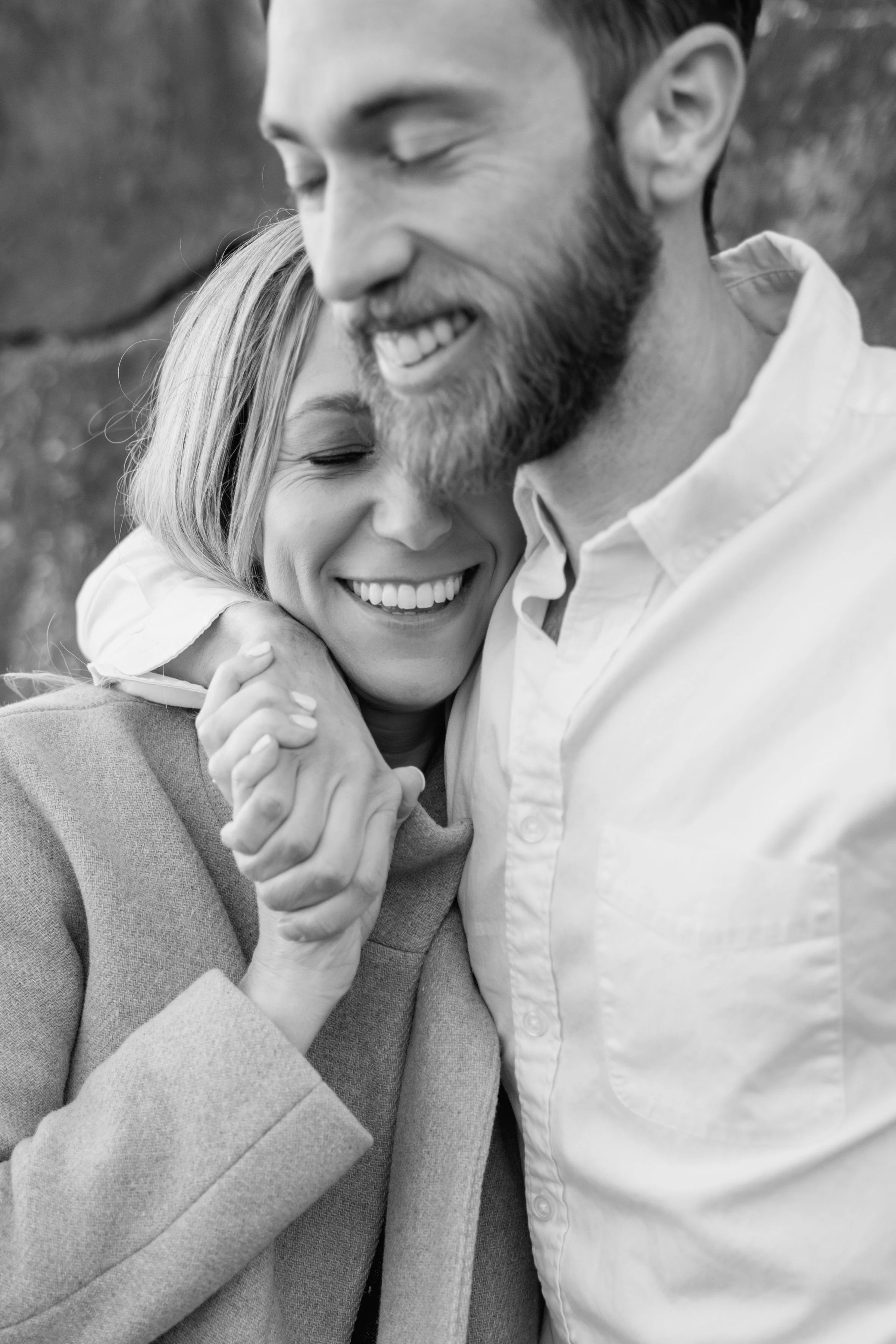 A black and white photo of a man and a woman smiling and hugging each other, with the woman gently resting her head on the man's chest.