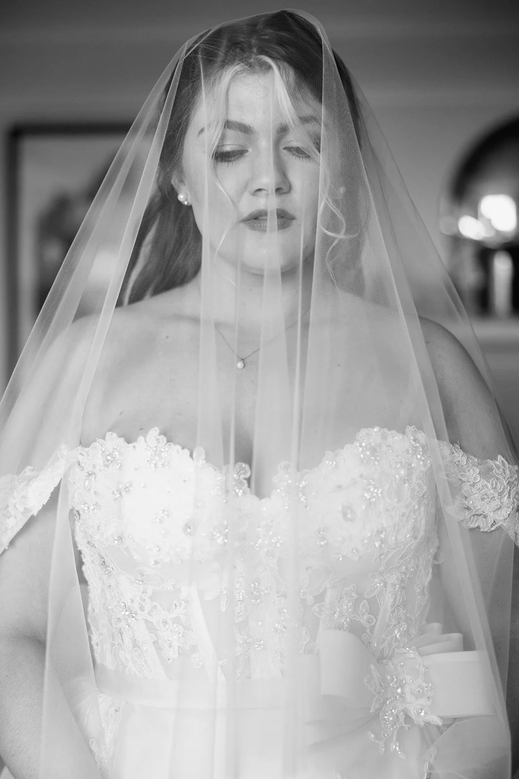 Black and white photo of a bride wearing a wedding dress and veil, with her eyes closed.