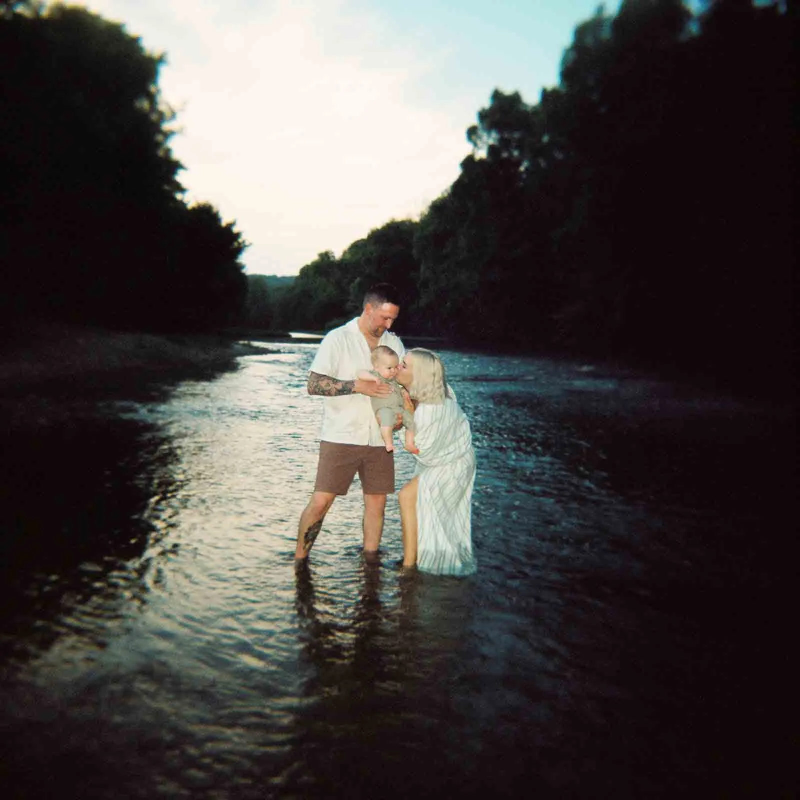 Family of three wearing white standing in the river playing