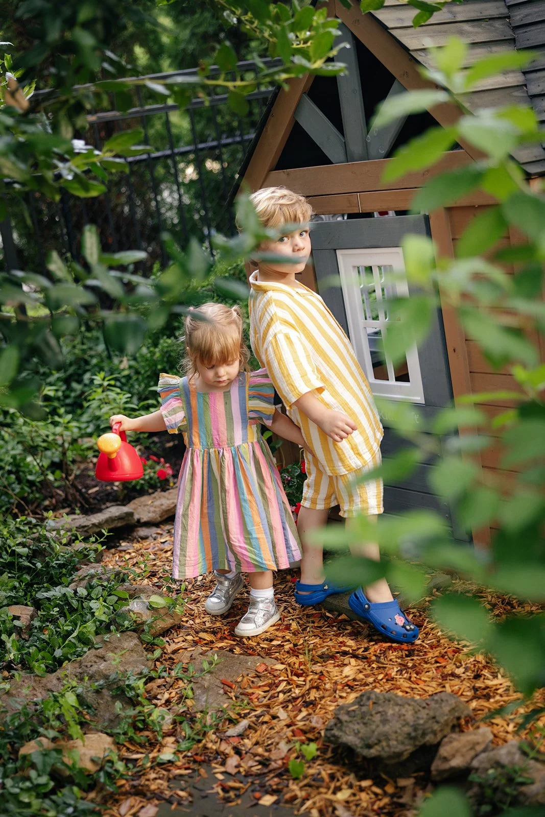 Two kids playing with toys outside next to a play house