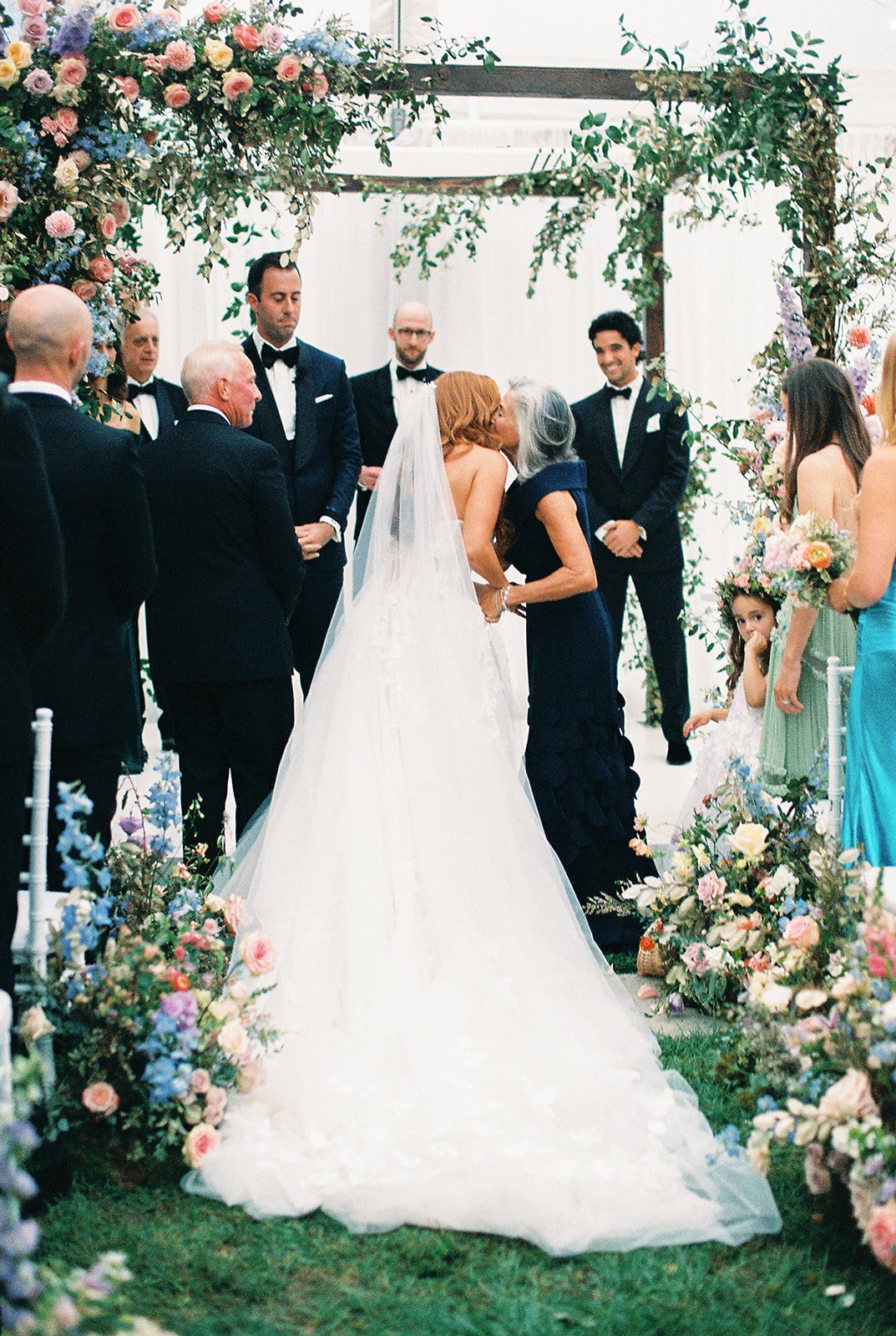 mom and daughter hugging while bride walks down the aisle to get married with colorful florals