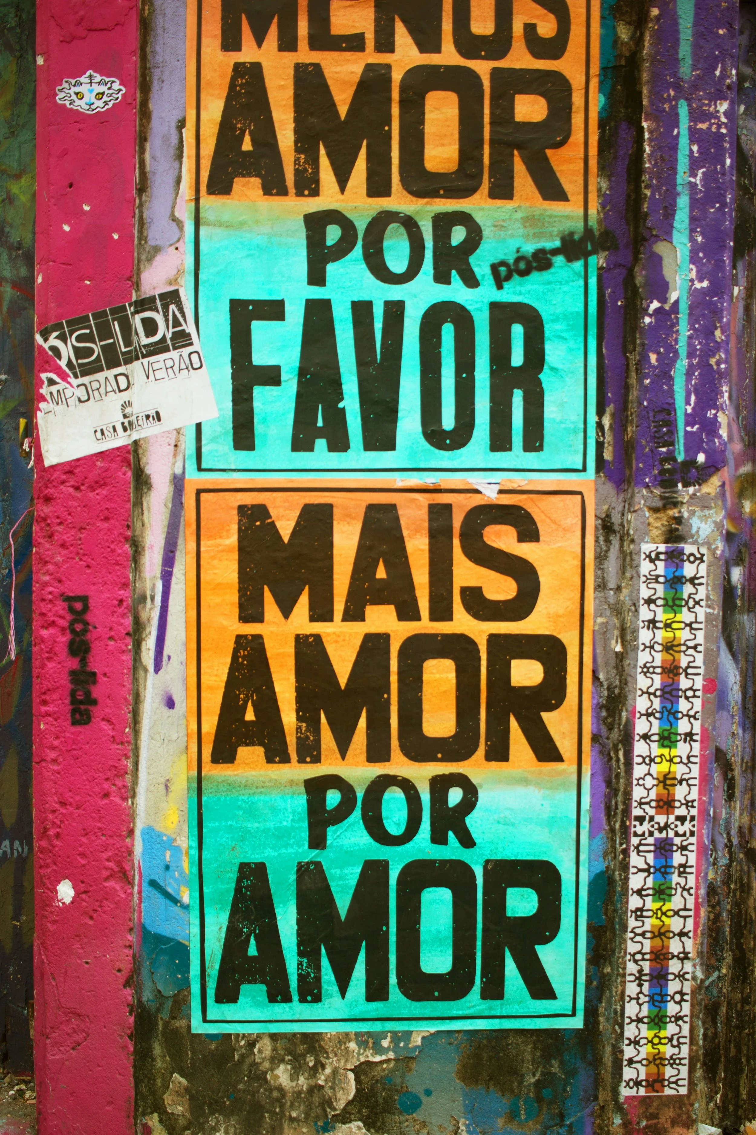 Colorful street posters with messages in Portuguese, saying 'Mais Amor Por Amor,' surrounded by sticker and graffiti embellishments.