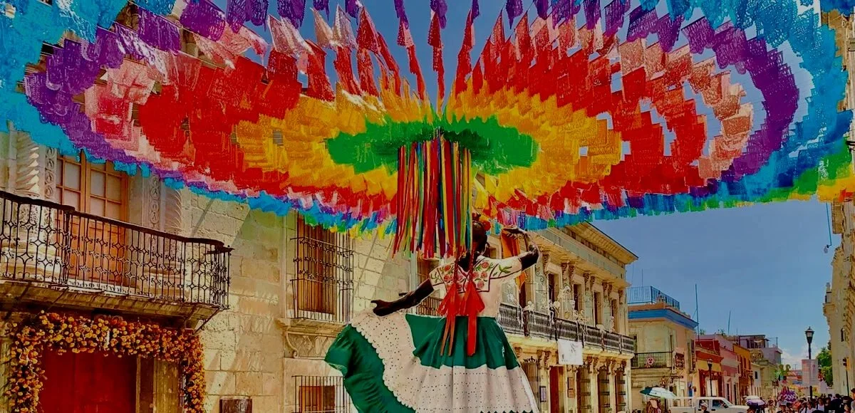 A street performer dressed in an elegant green and white dress, performing a dance under a colorful, large parasol with rainbow patterns in a lively city street.