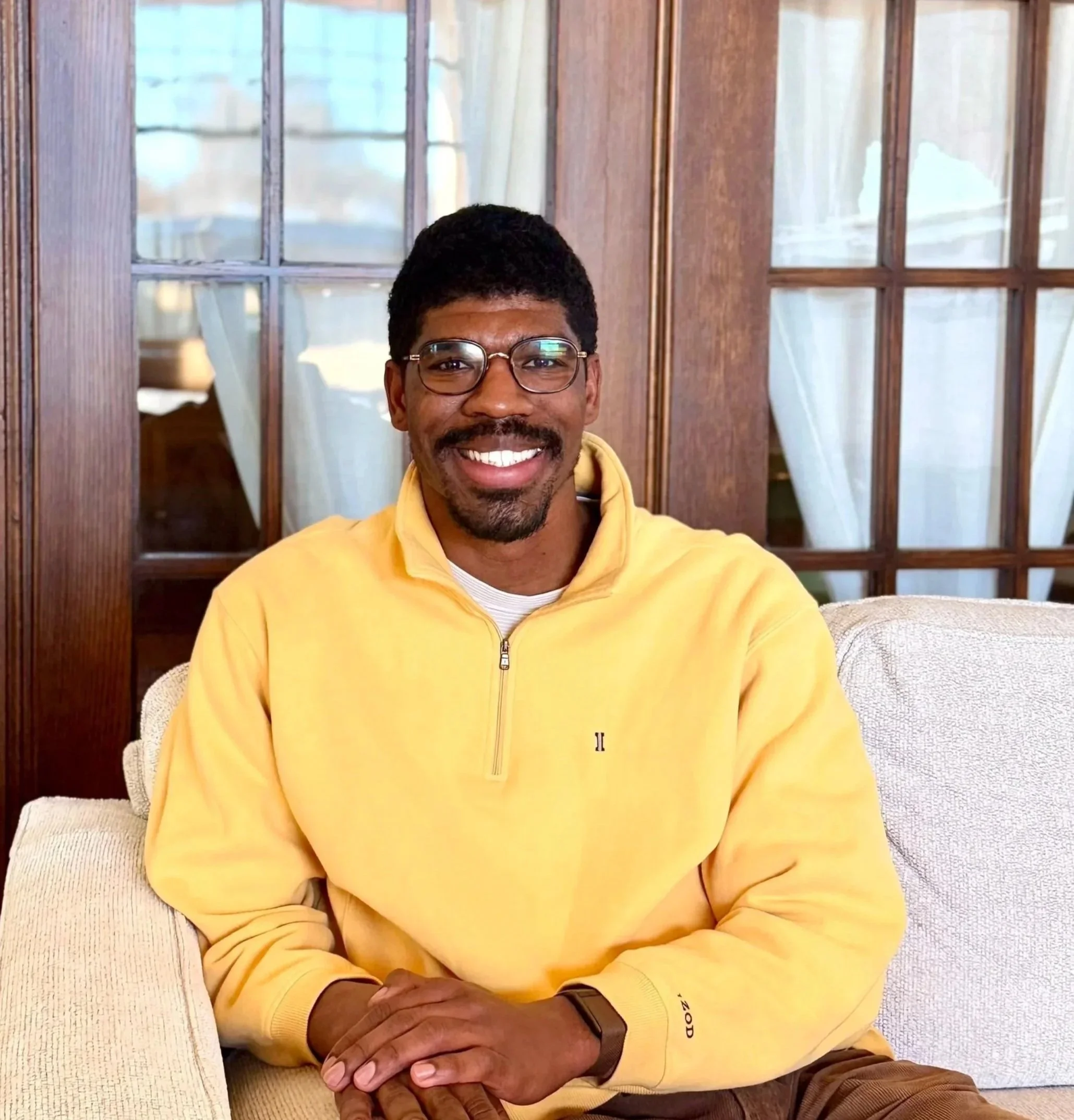 Young man with glasses in a white shirt and maroon graduation stole amid fall foliage.