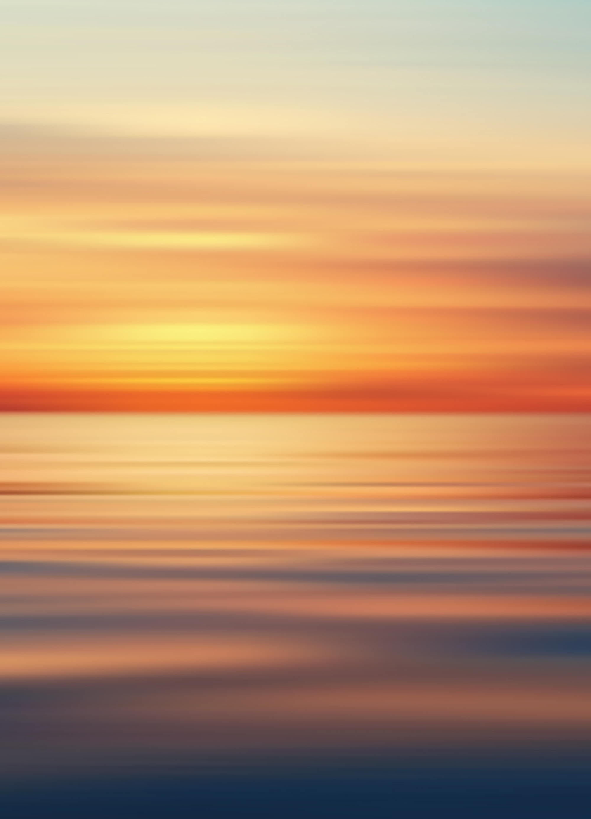 Blurred image of a colorful sunset over the ocean with hues of orange, yellow, pink, and blue.