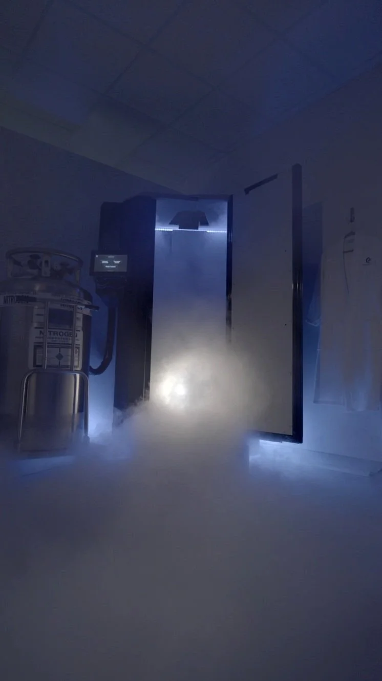 A hospital or medical facility corridor with a door emitting blue light and fog or vapor on the floor, alongside medical equipment on the left.