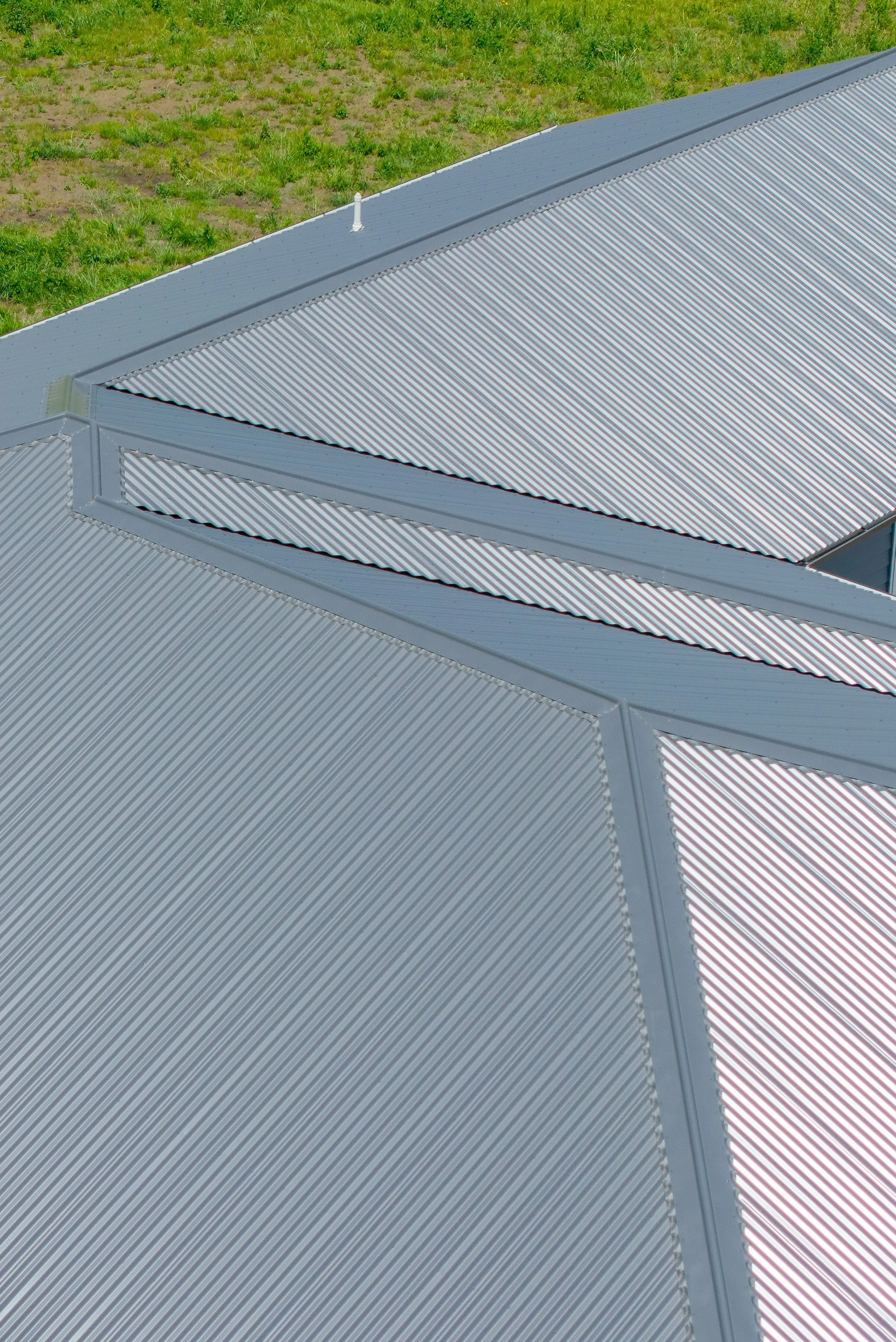 Close-up view of a metal roof with ridges, set against a grassy background.