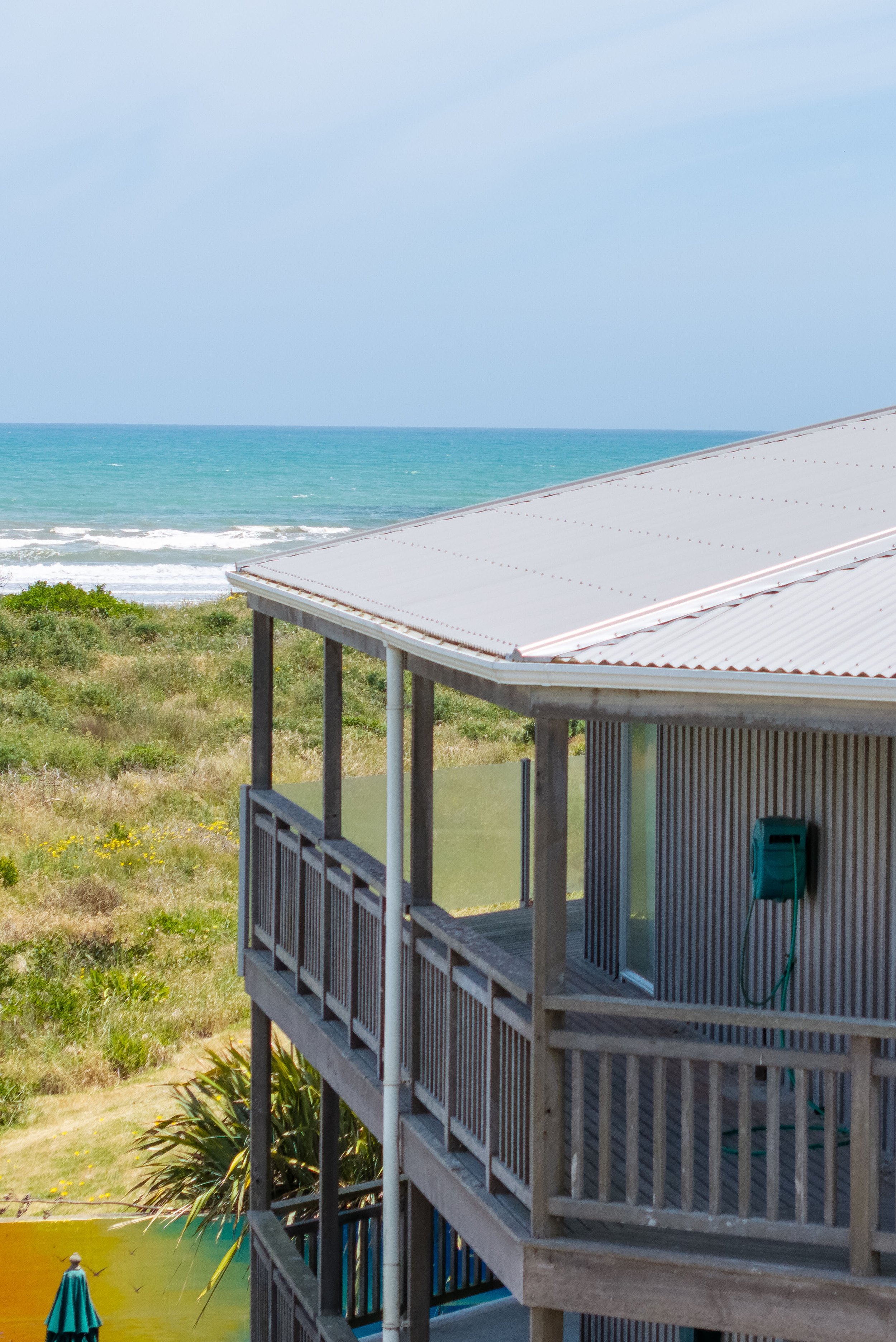 Beach house with a balcony overlooking a grassy area and the ocean in the background.