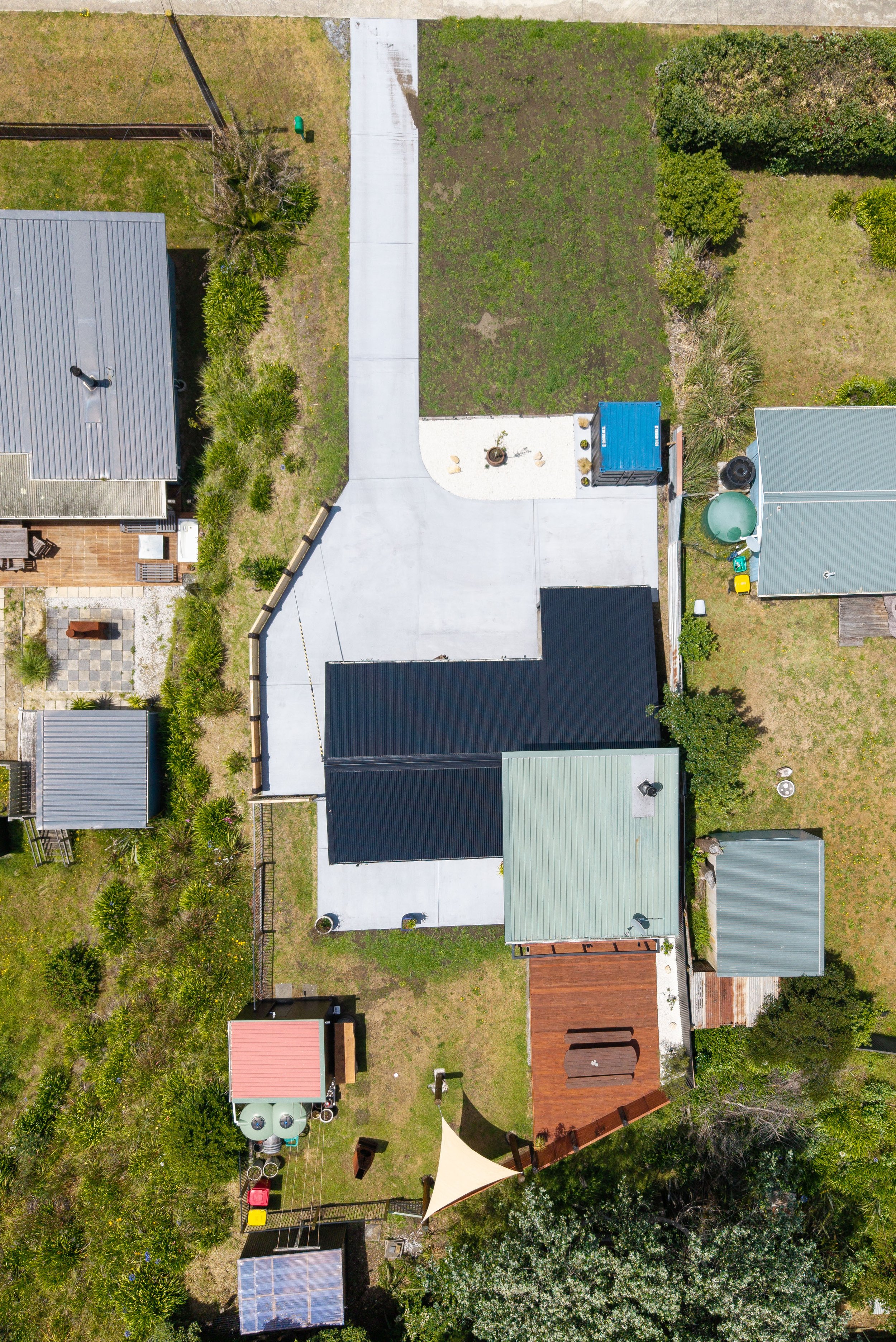 Aerial view of a backyard with various structures, green grass areas, some trees, and a driveway.