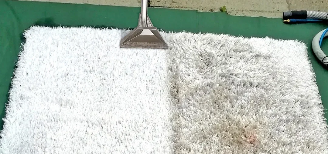 A white fluffy cleaning cloth on a green surface with a metal squeegee and vacuum hose visible.